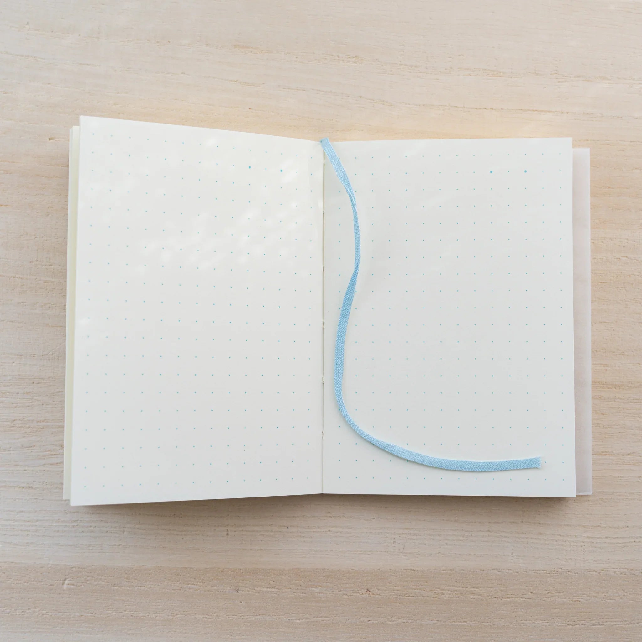 MD Notebook A7 opened flat with a blue bookmark ribbon across a cream spread