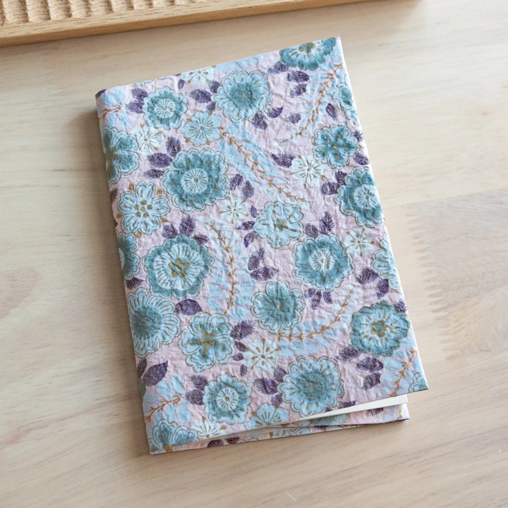 Pastel pink hand-dyed yuzen washi book cover A6, closed view showing floral embroidered pattern, overhead composition