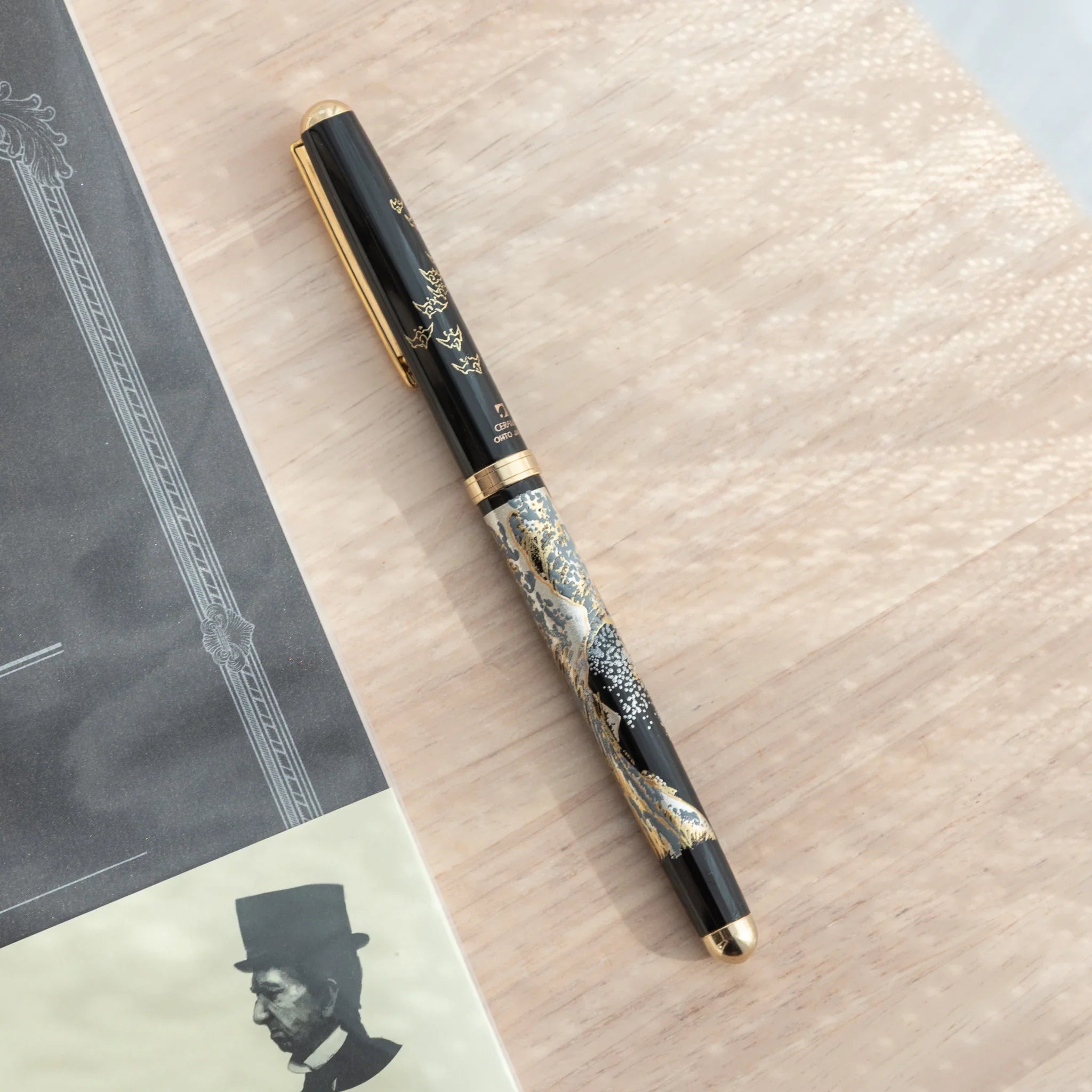 Maeju Yamanaka ballpoint pen, black barrel with Great Wave silkscreen in silver and gold, gold clip and cap, on wood surface