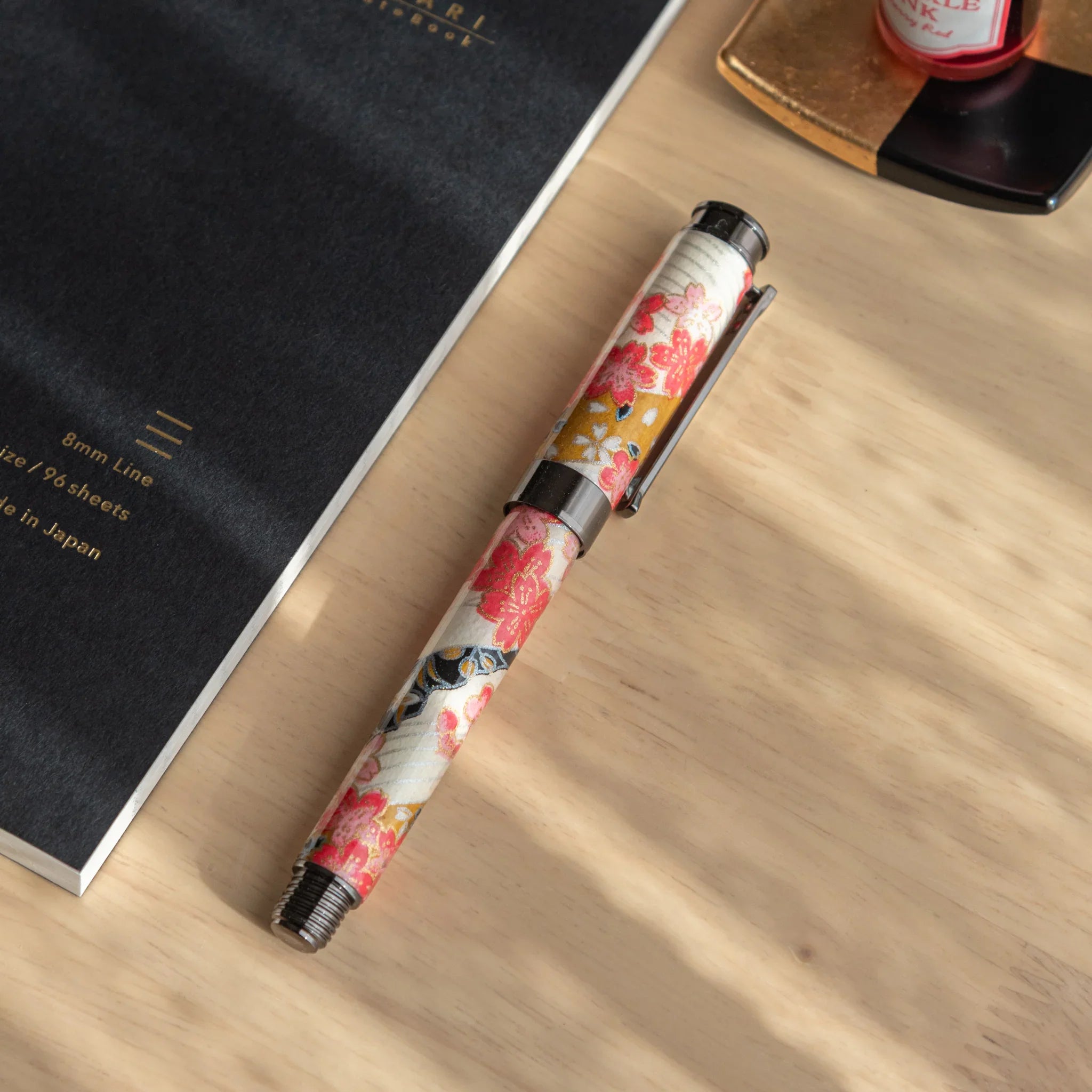 Akebono Cherry Mino washi fountain pen on YU-SARI notebook with red cherry blossoms and gold accents angled view