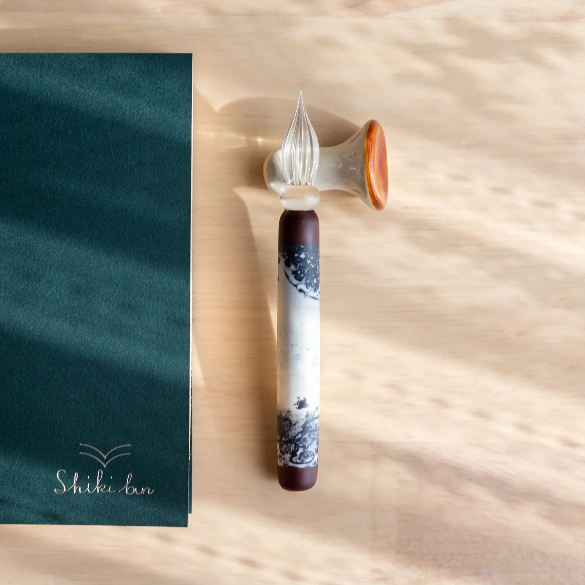 Orange and white mushroom-shaped pen rest with glass dip pen displayed on open journal and fabric background shine