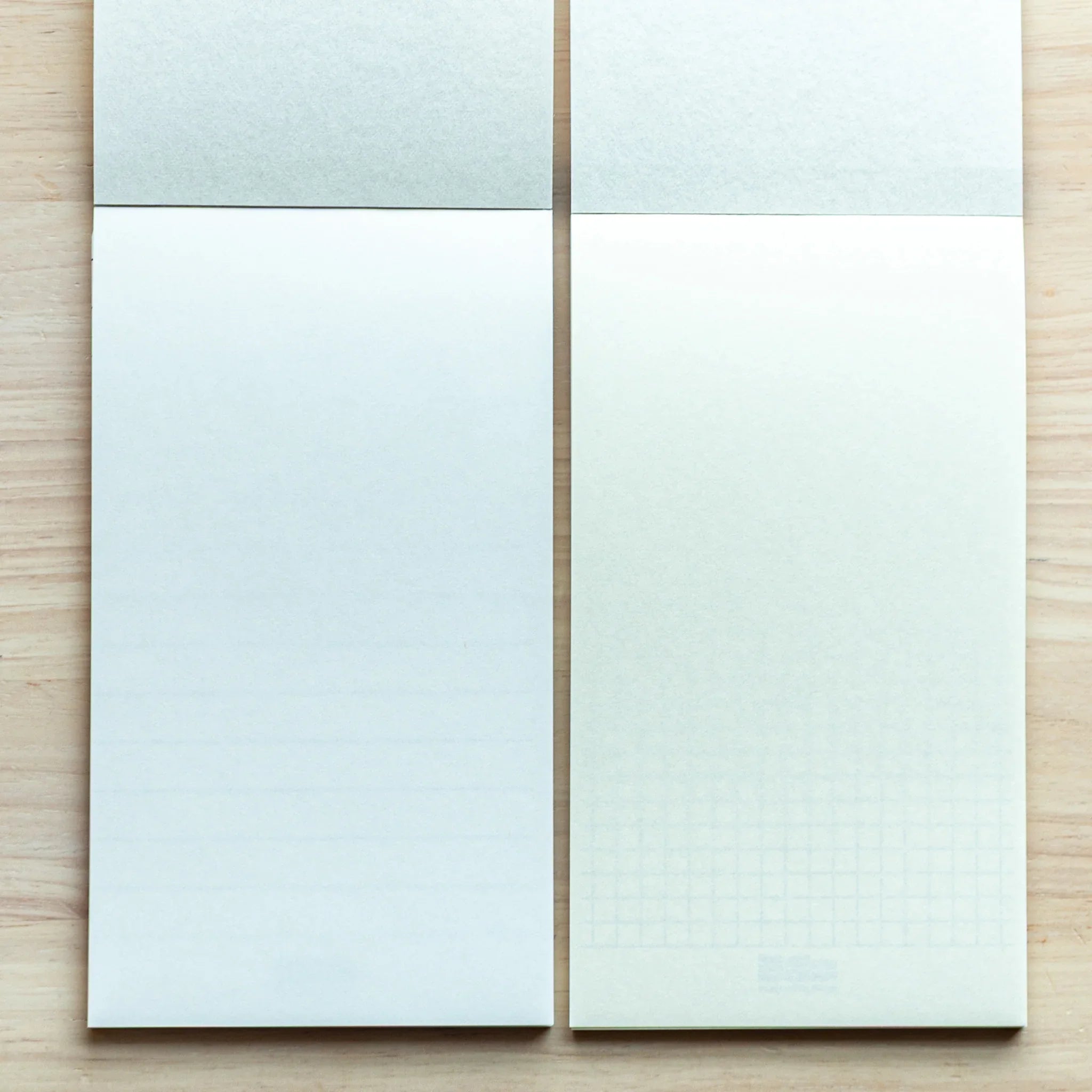 Two Bullet Jotter writing pads on light wood, blank pages: left light blue-tinted, right faint cream-tinted paper