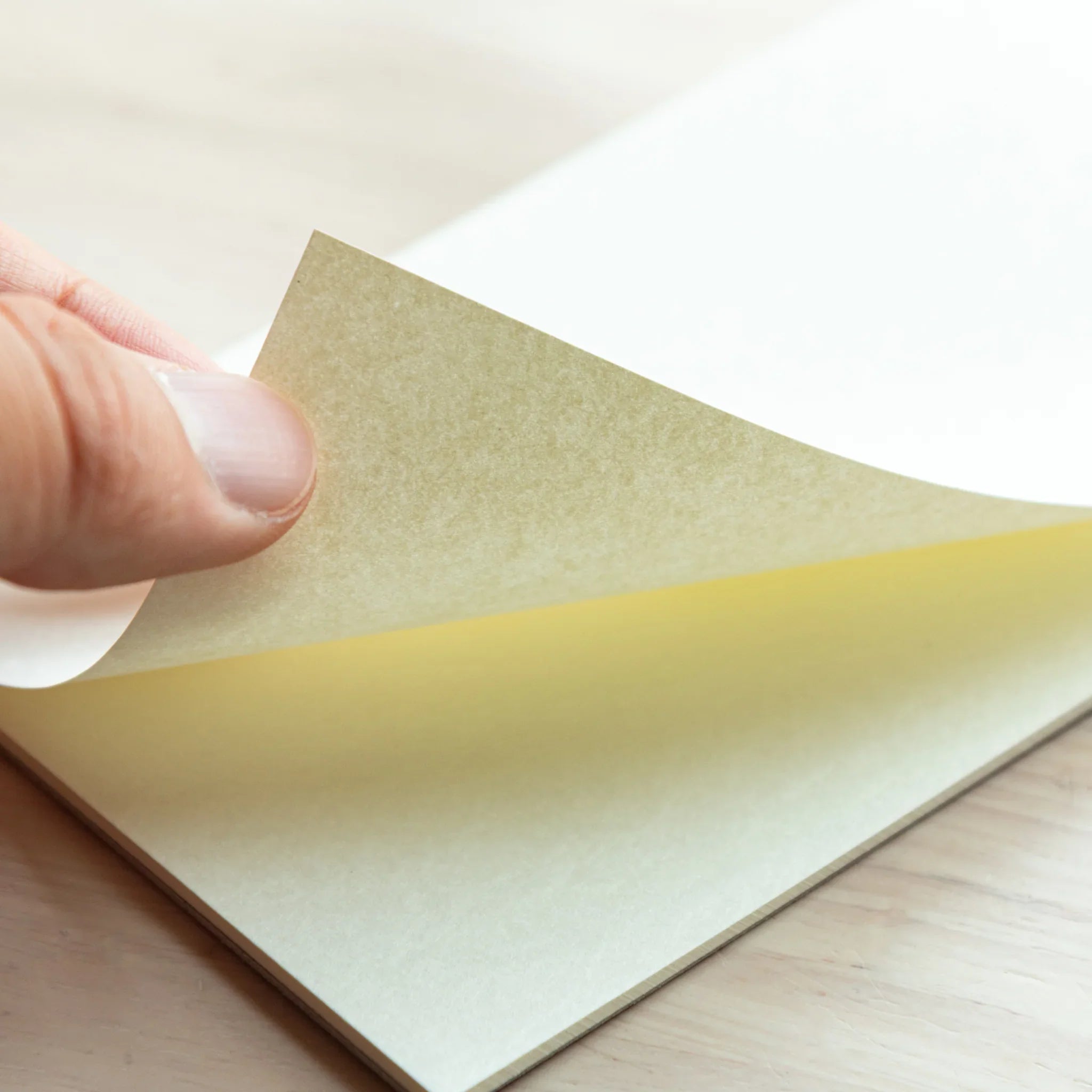 Hand peeling a page from Bullet Jotter writing pad, revealing yellow glue spine and light-tinted Sheep Clouds Bond paper
