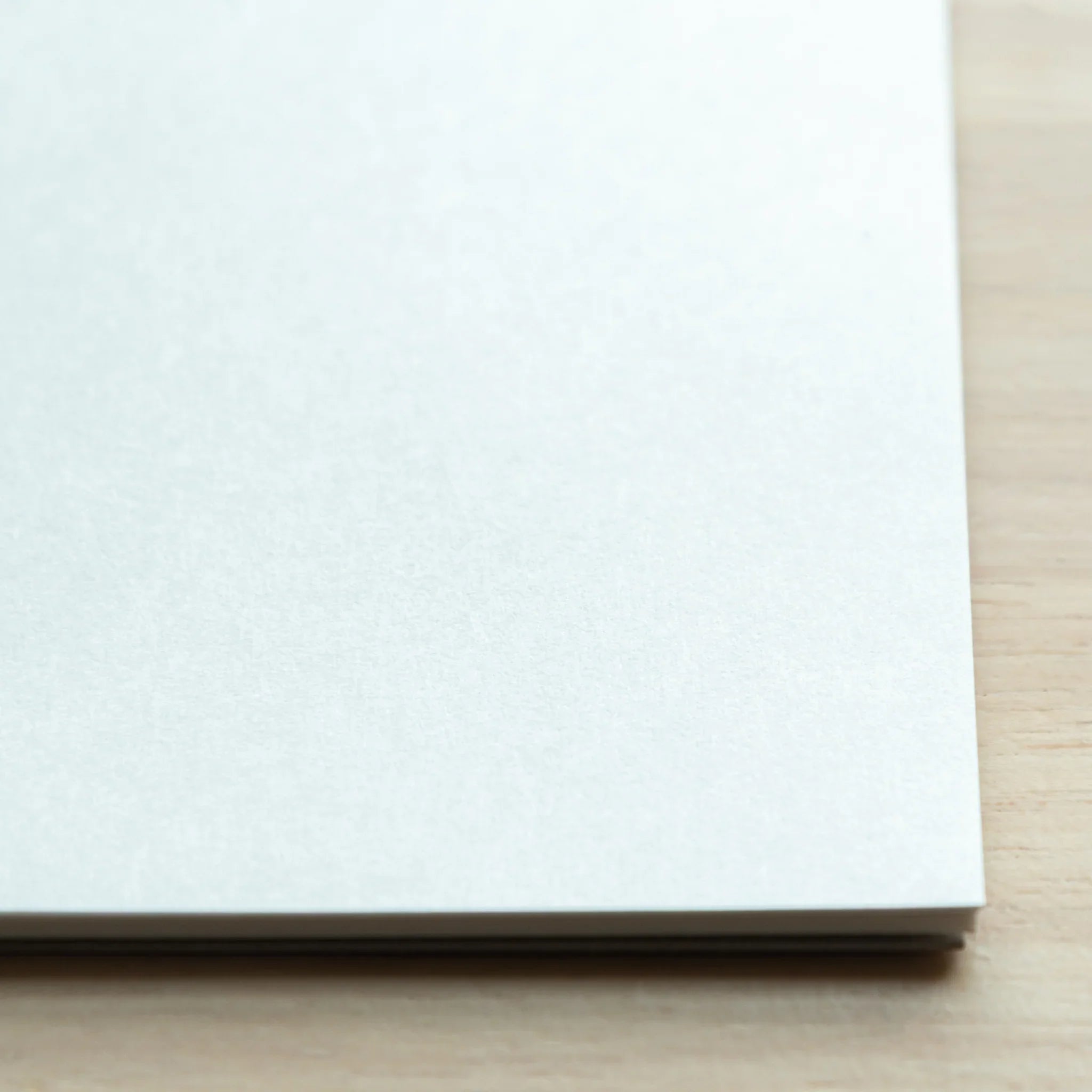 Close-up corner view of Soliste writing pad on light wood, bright white paper surface and stacked sheet edges visible