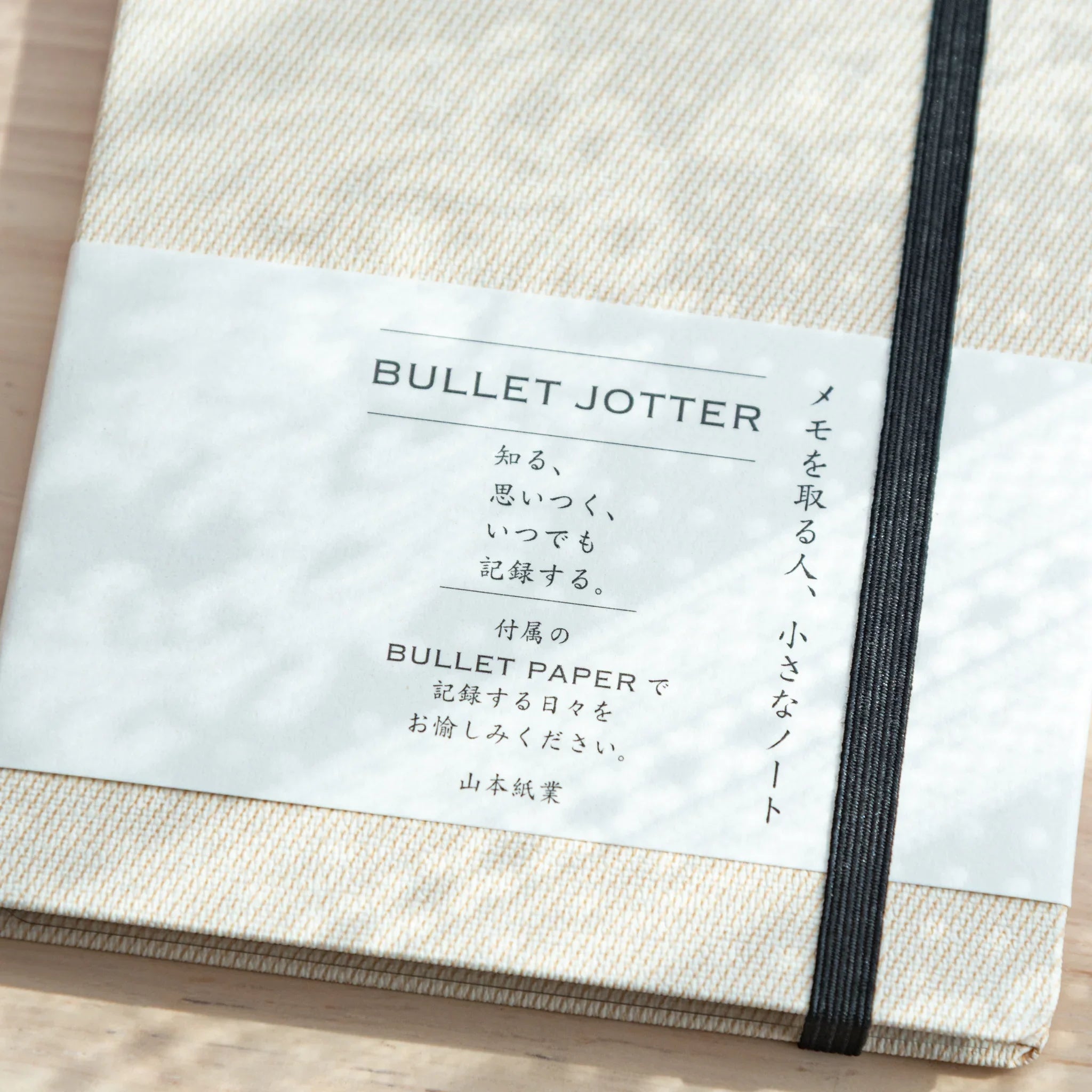 Close-up of Bullet Jotter ivory white cover belly band: BULLET JOTTER title, Japanese description, black elastic band
