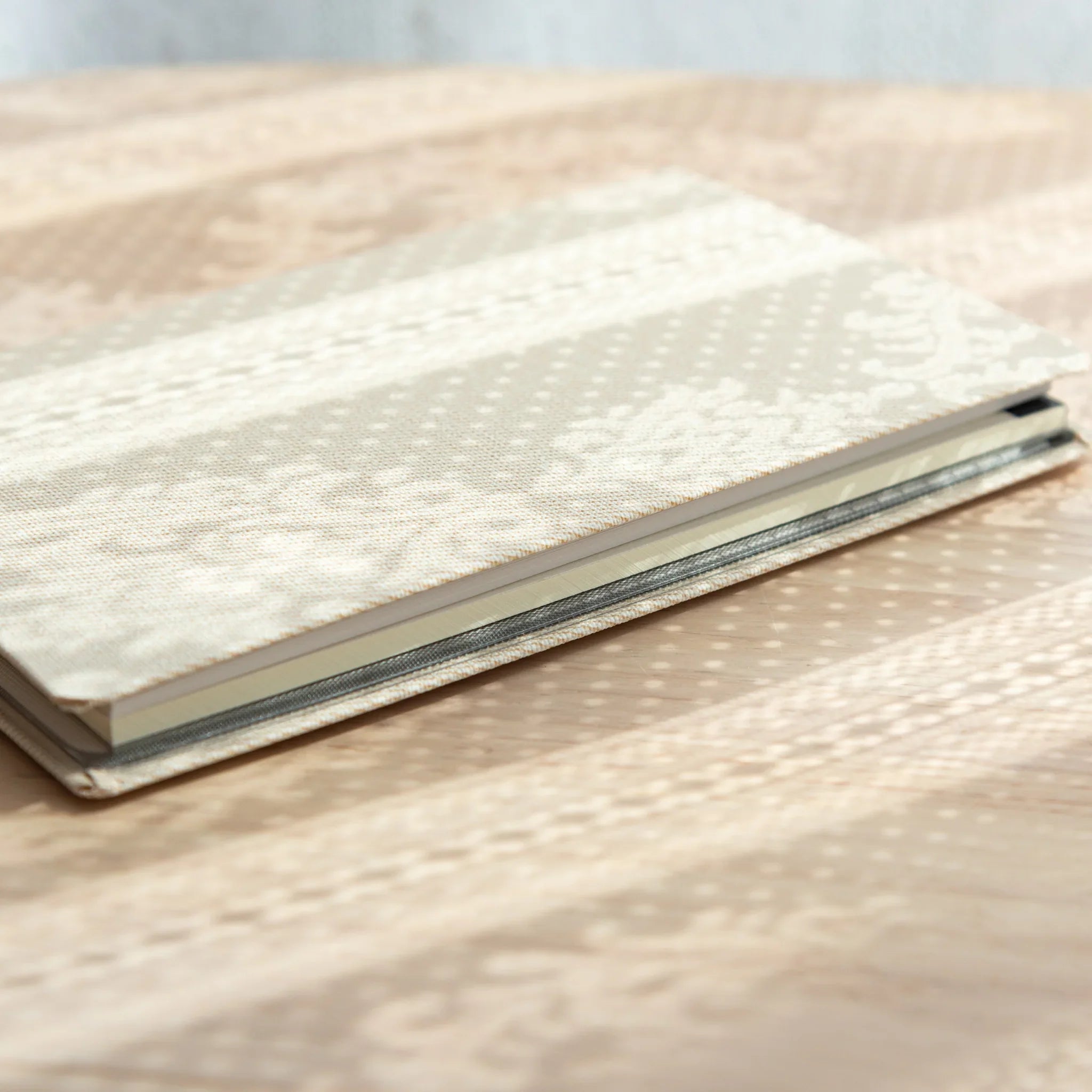 Angled side view of closed Bullet Jotter ivory white gabardine cover on textured surface, sheet edges visible at right