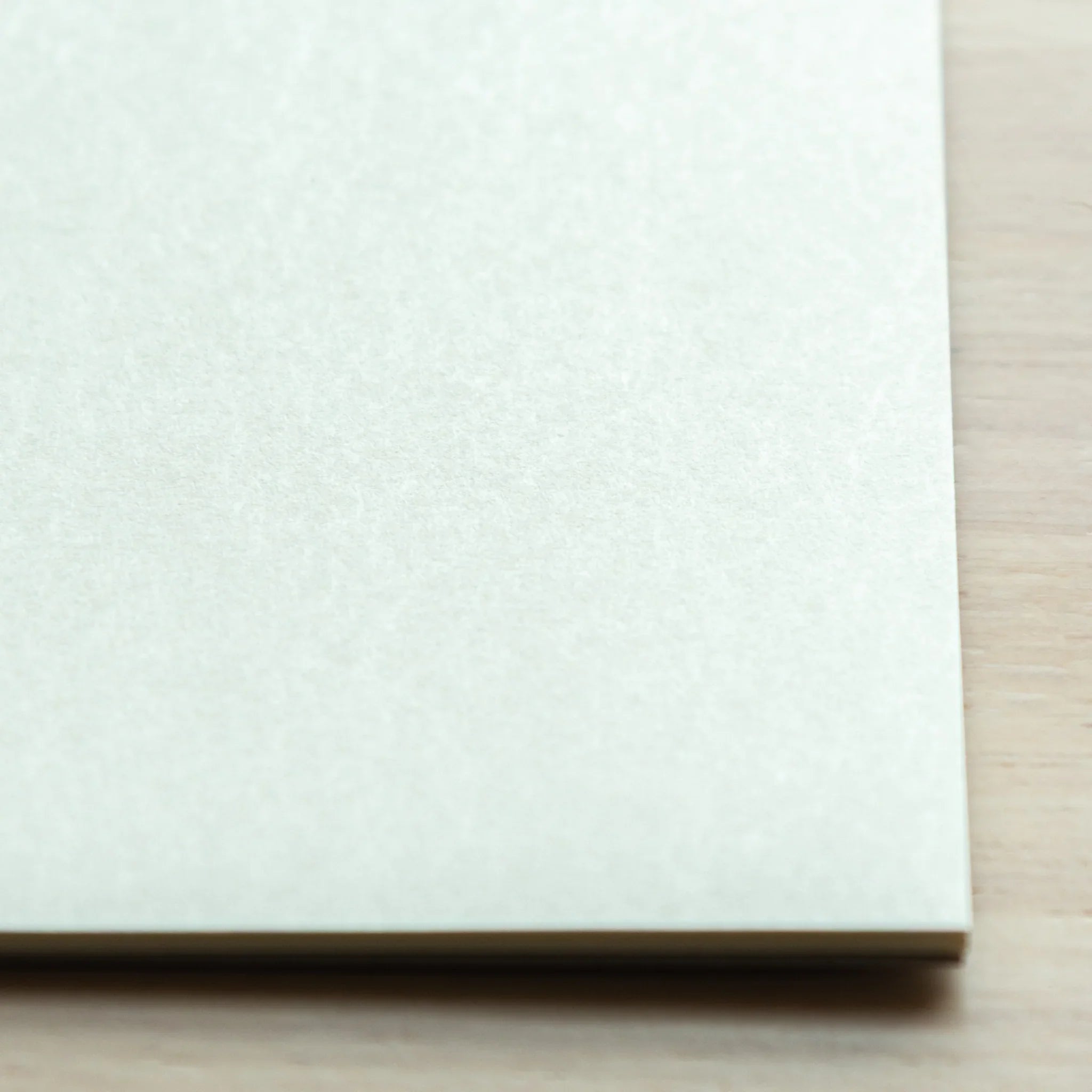 Close-up bottom corner of Bullet Jotter writing pad on wood surface, showing white paper texture and stacked sheet edges