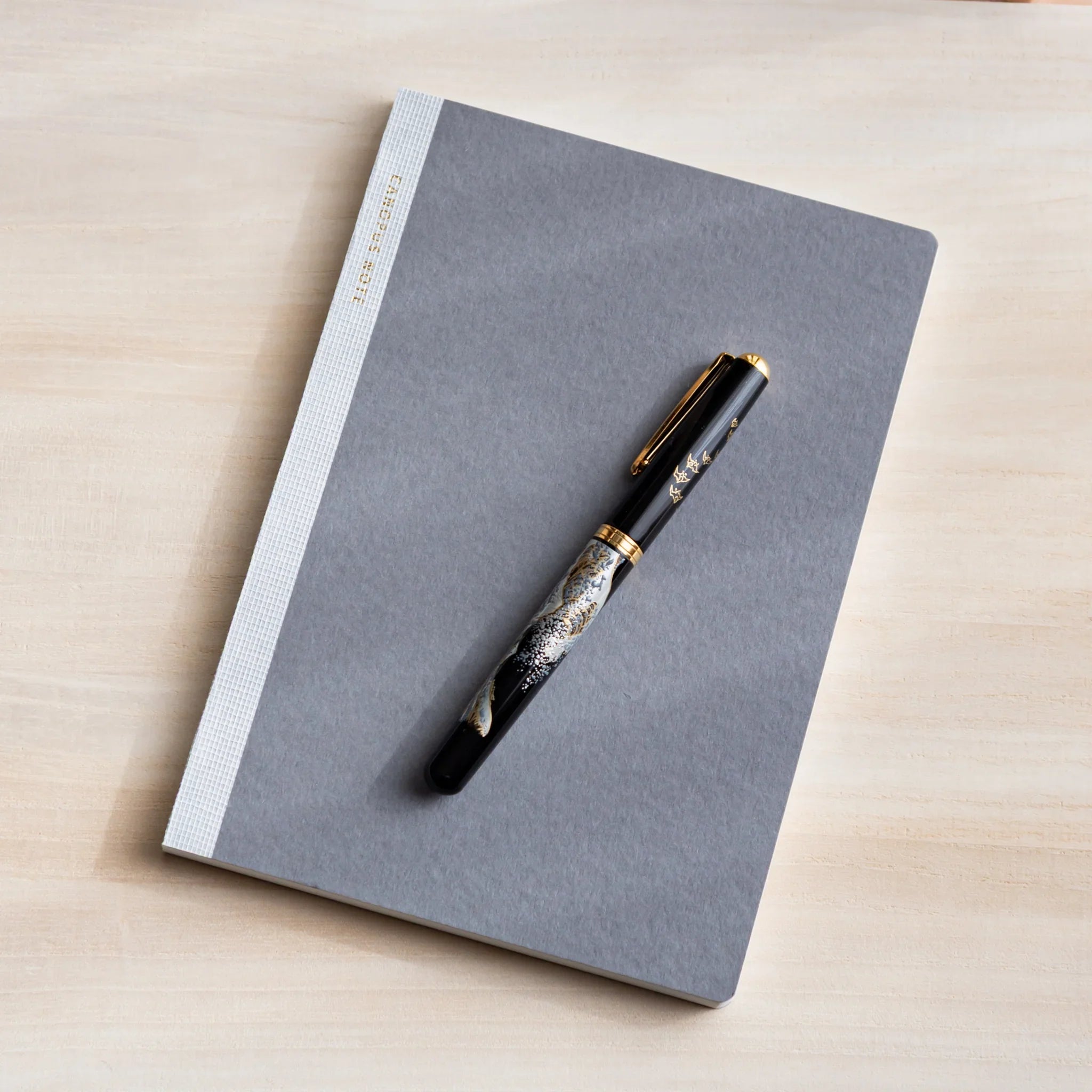 Flat lay of CANOPUS notebook with pen on wooden desk surface showing product quality and design details