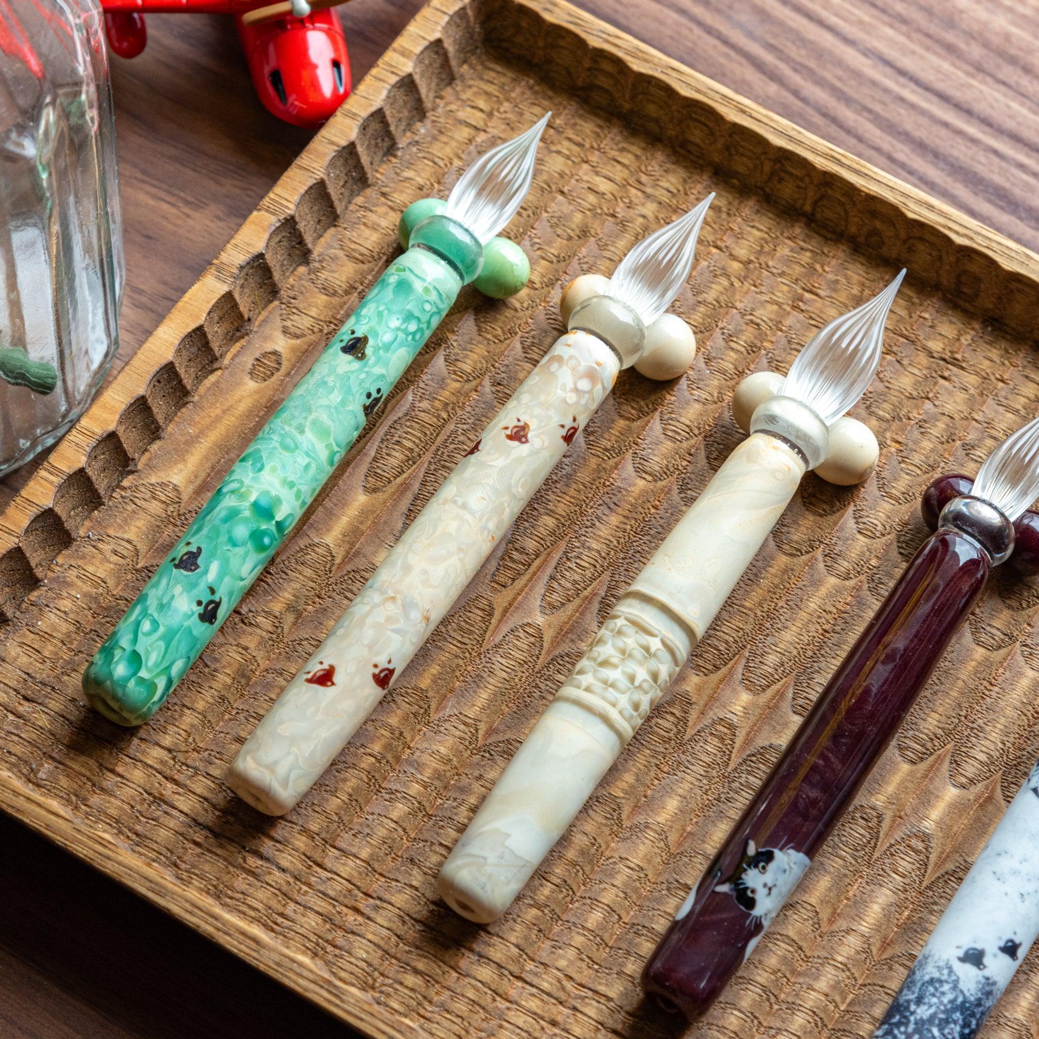Overhead product display showing ivory glass dip pen among other pens in wooden tray collection arrangement set