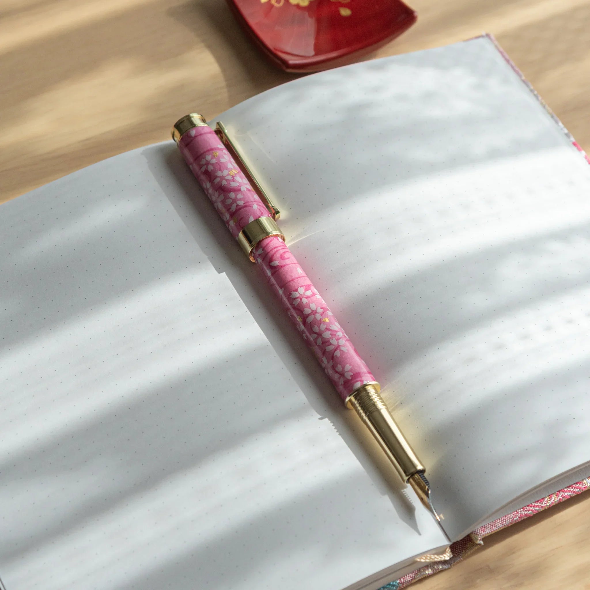 Pink Mino washi Japanese fountain pen with white sakura print resting on an open notebook with dot-grid white pages