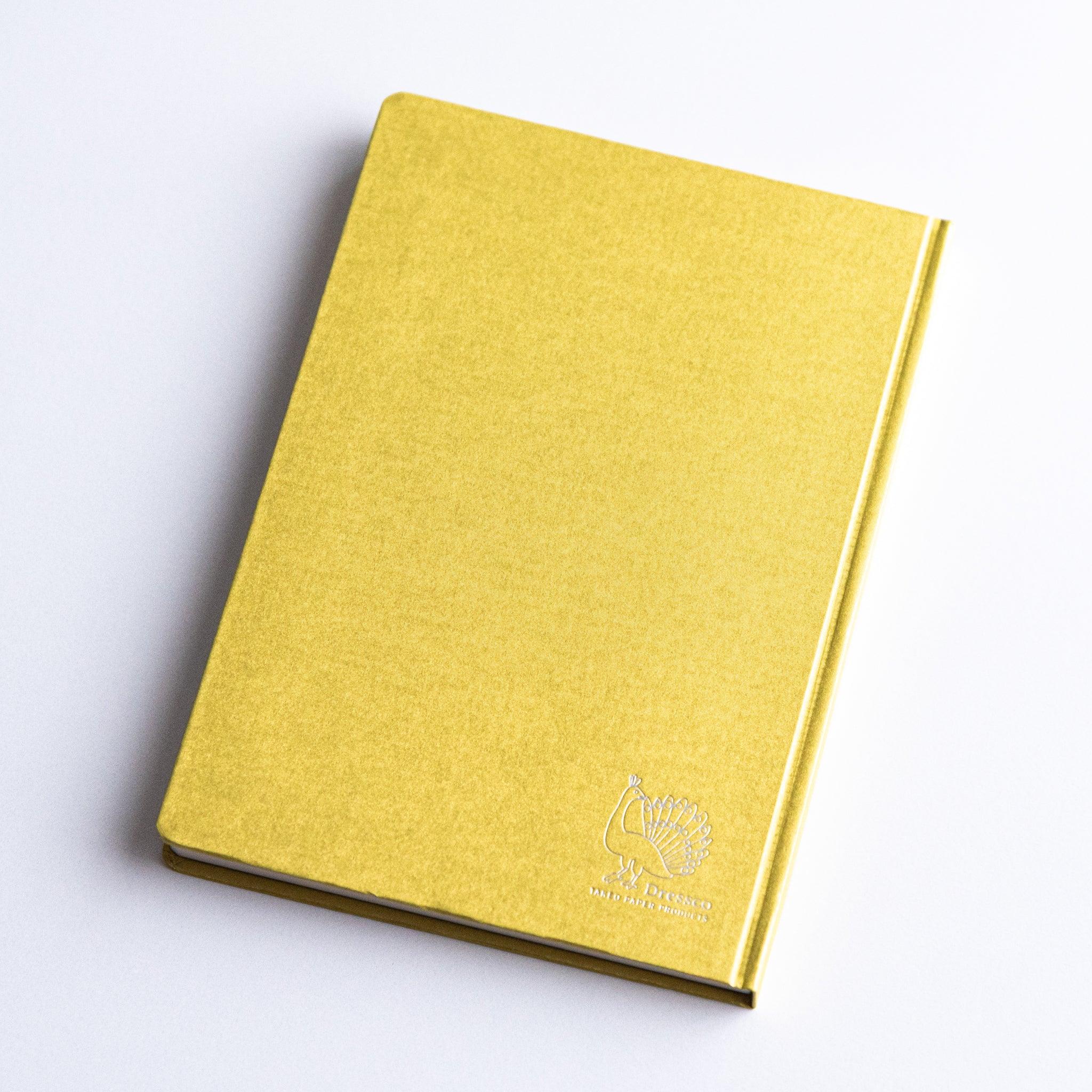 Dressco Bank Ledger Paper A6 notebook in flat composition showing the cover face and spine edge from side angle