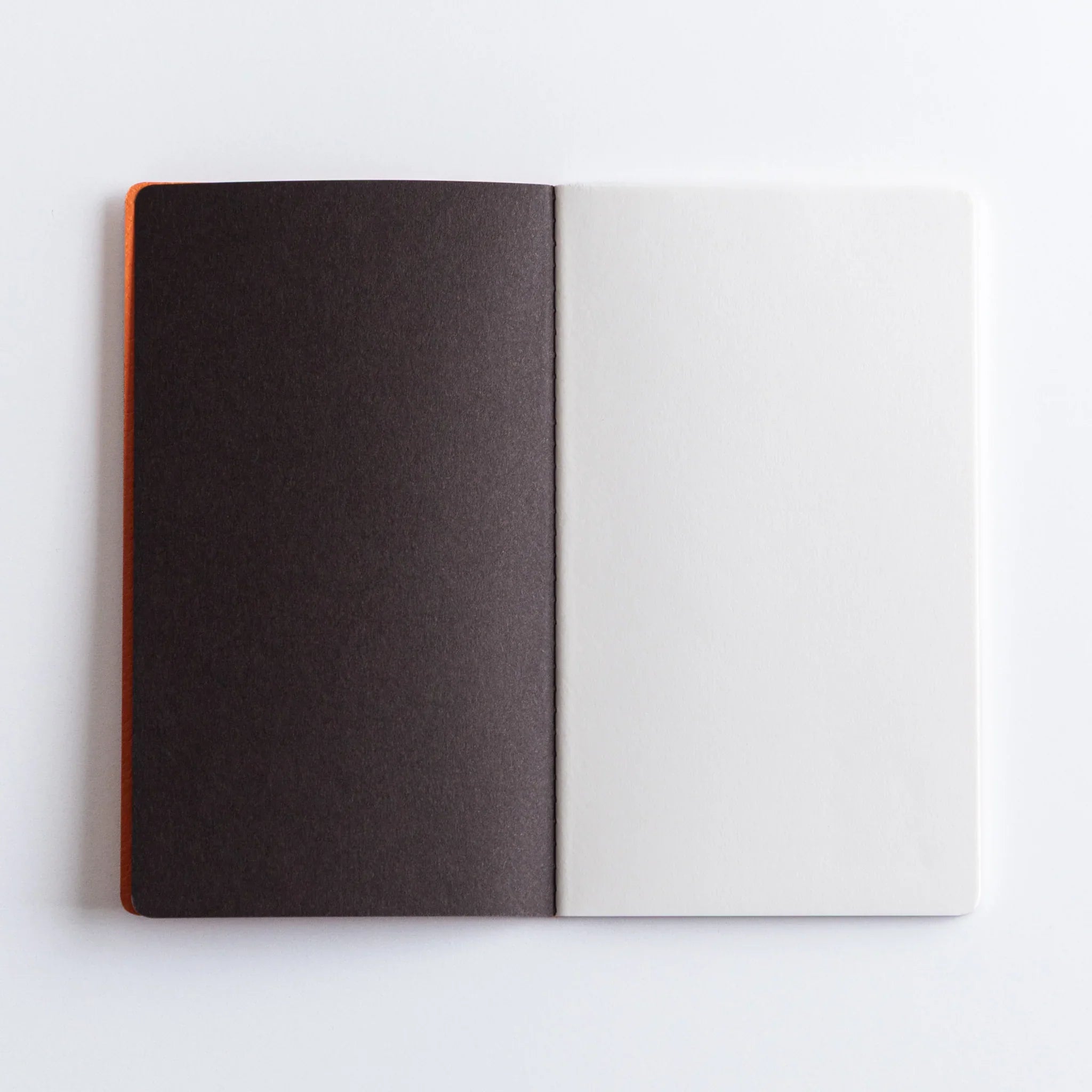 Charcoal and orange Dressco notebooks stacked together showing page thickness and stitched binding along notebook edge
