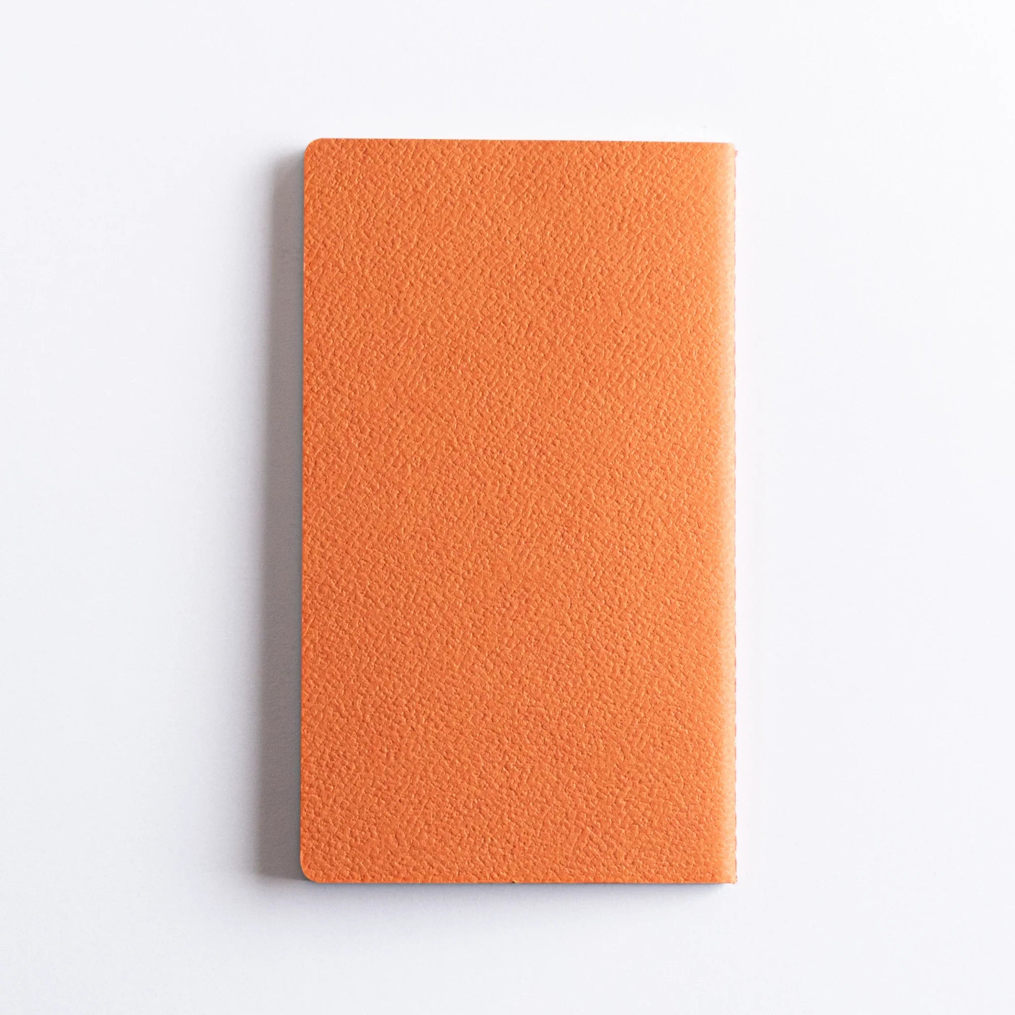 Single orange A6 Dressco stitched notebook with textured fabric cover displayed on plain white background surface