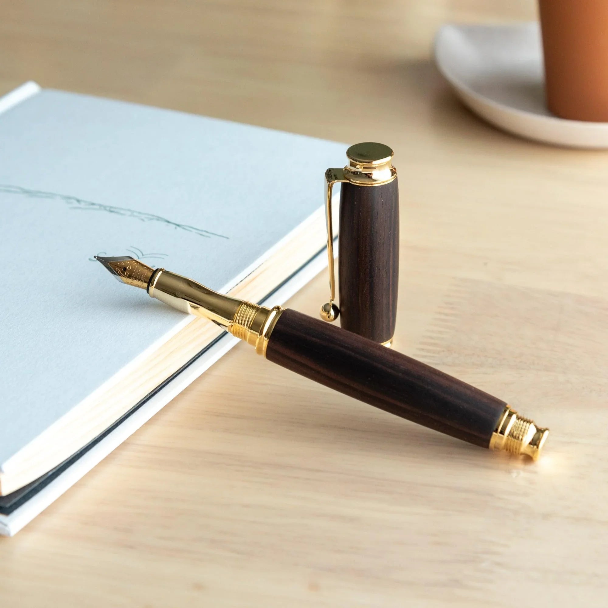 Japanese ebony wood fountain pen with gold band trim and screw cap resting on white paper surface displayed clearly