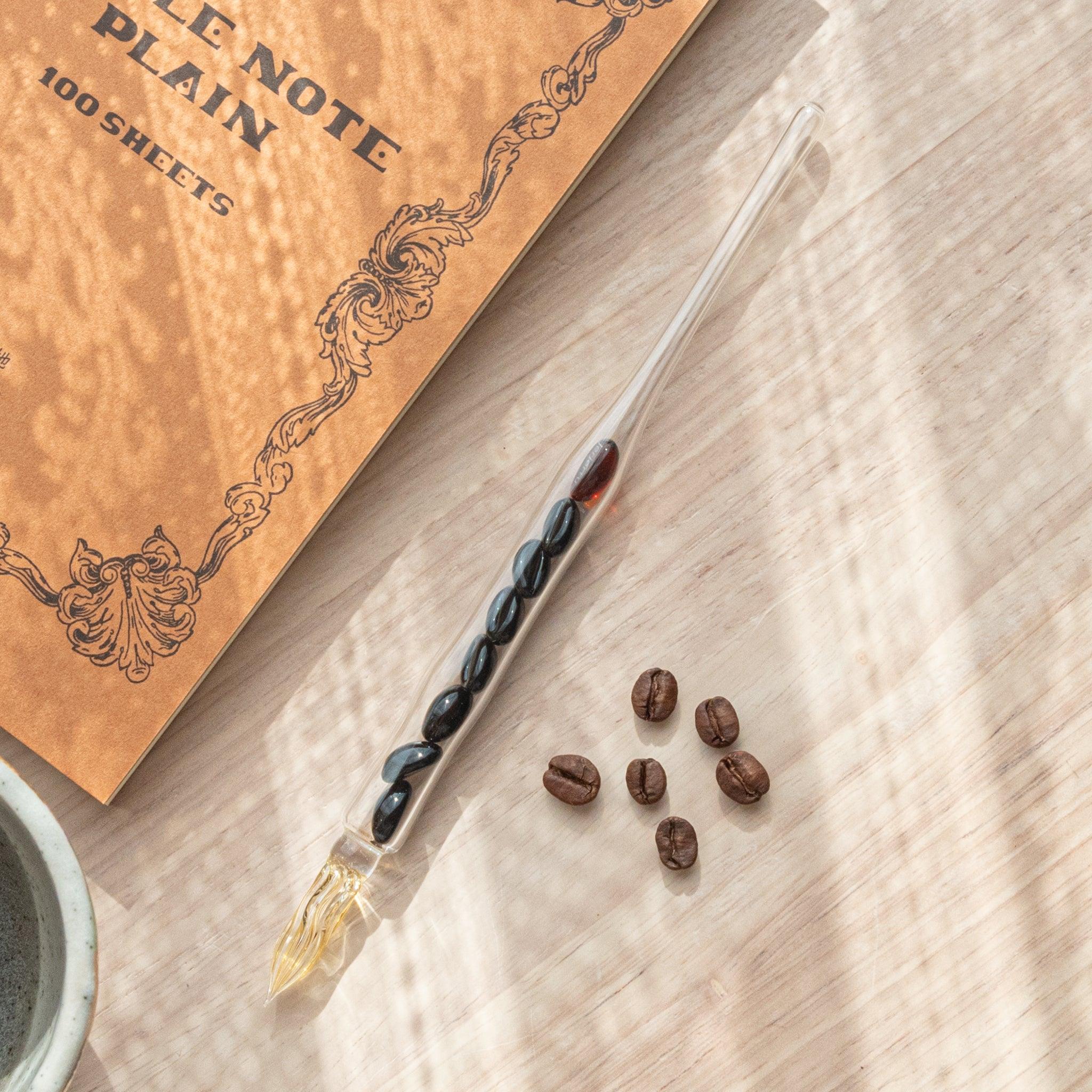 French Roast Coffee Beans Glass Dip Pen with matching dark coffee-themed ink cartridge and decorative notepad on surface
