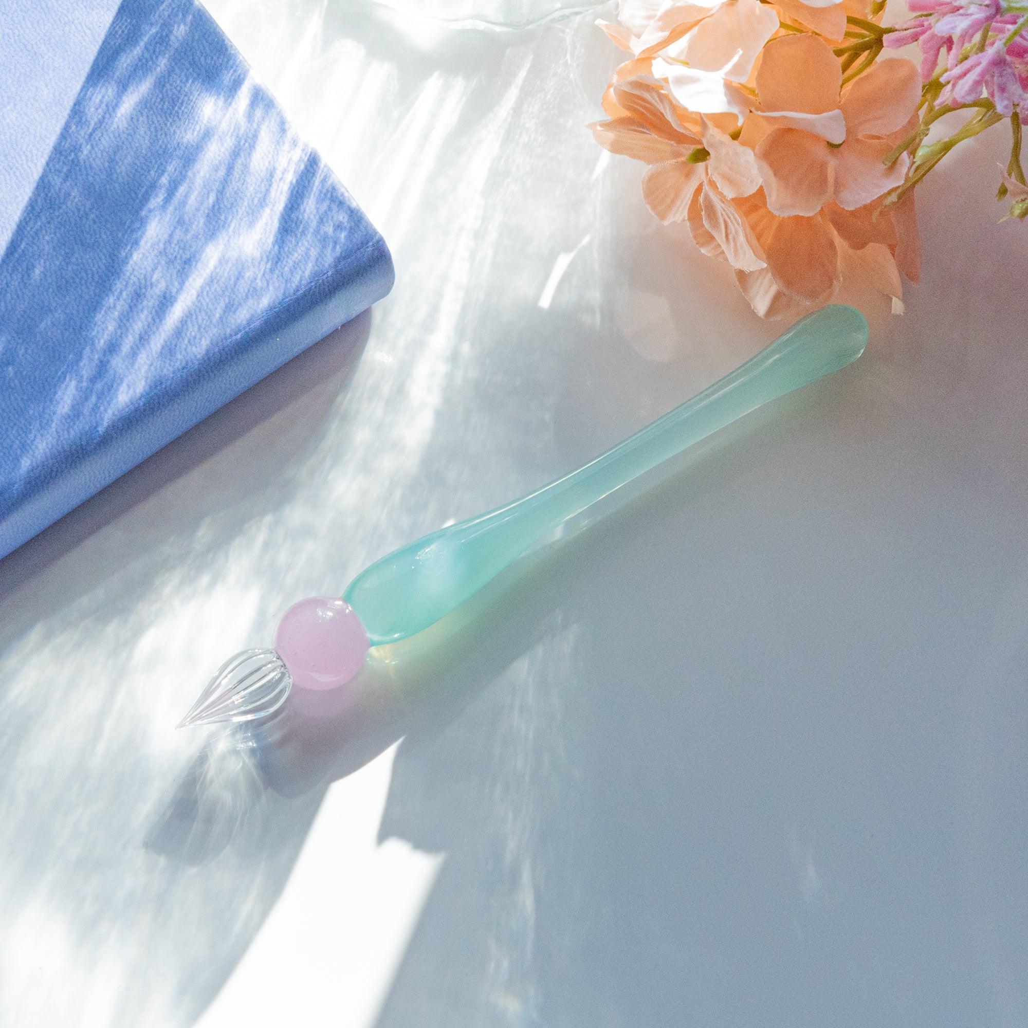 Mint green glass dip pen with pink spherical bead and clear fluted nib on white background with handle detail and decorative