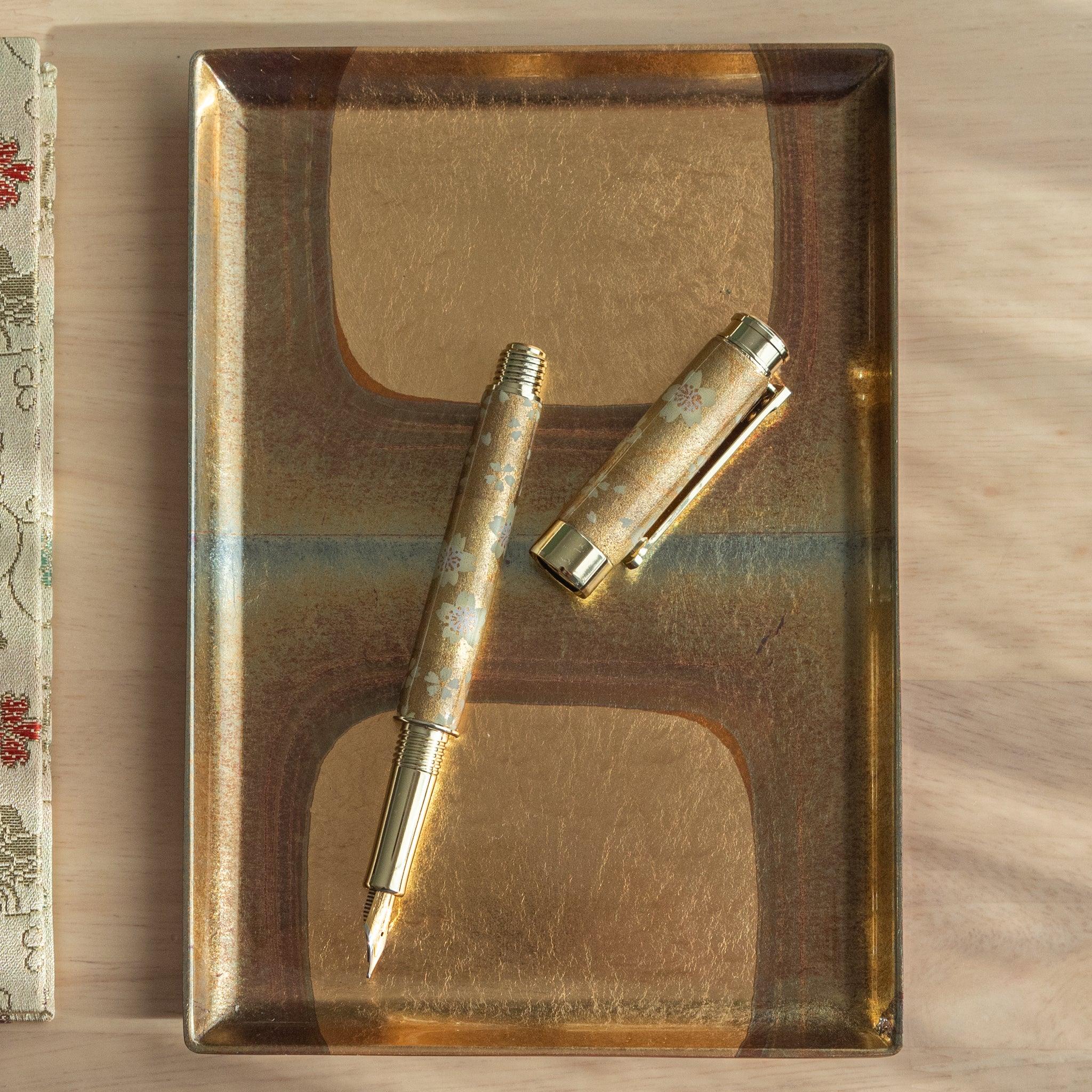 Gold Sakura Mino Washi fountain pen displayed on botanical background showing intricate cream wrapper with small gold flowers