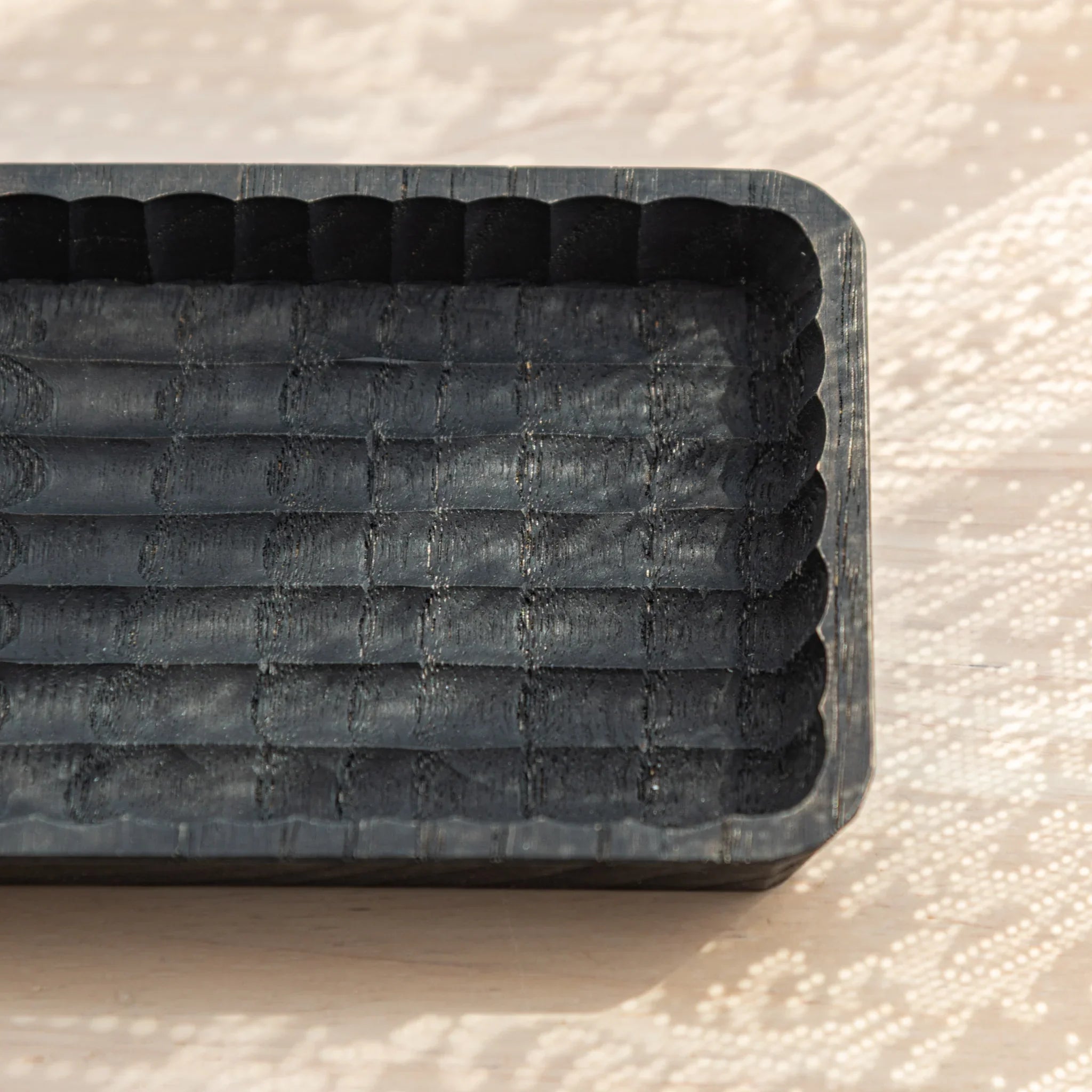 Empty charcoal Japanese pen tray close-up showing parallel groove texture and scalloped rim on patterned linen