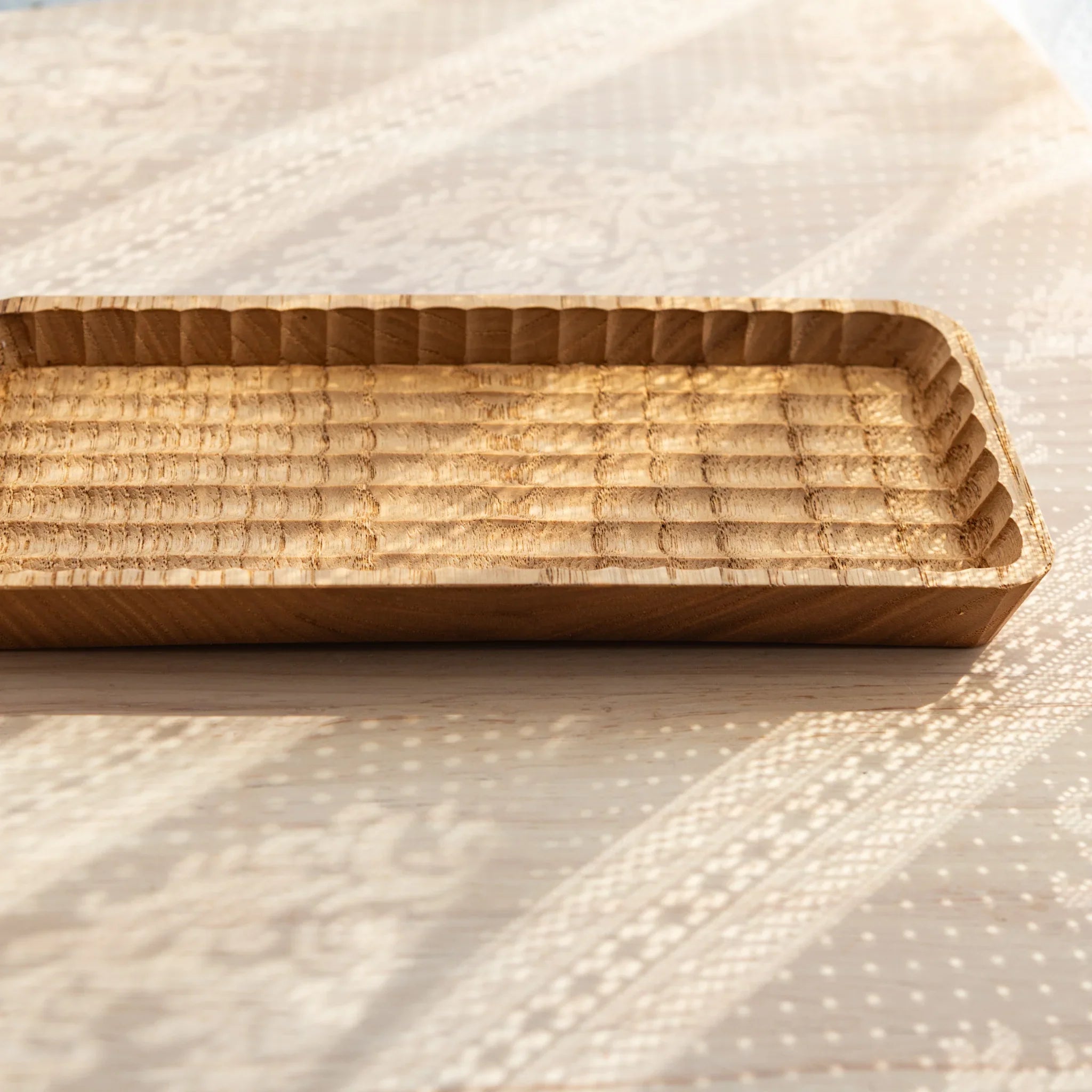 Empty light wood Japanese pen tray on patterned linen, showing groove carving and rounded corners from an angled view