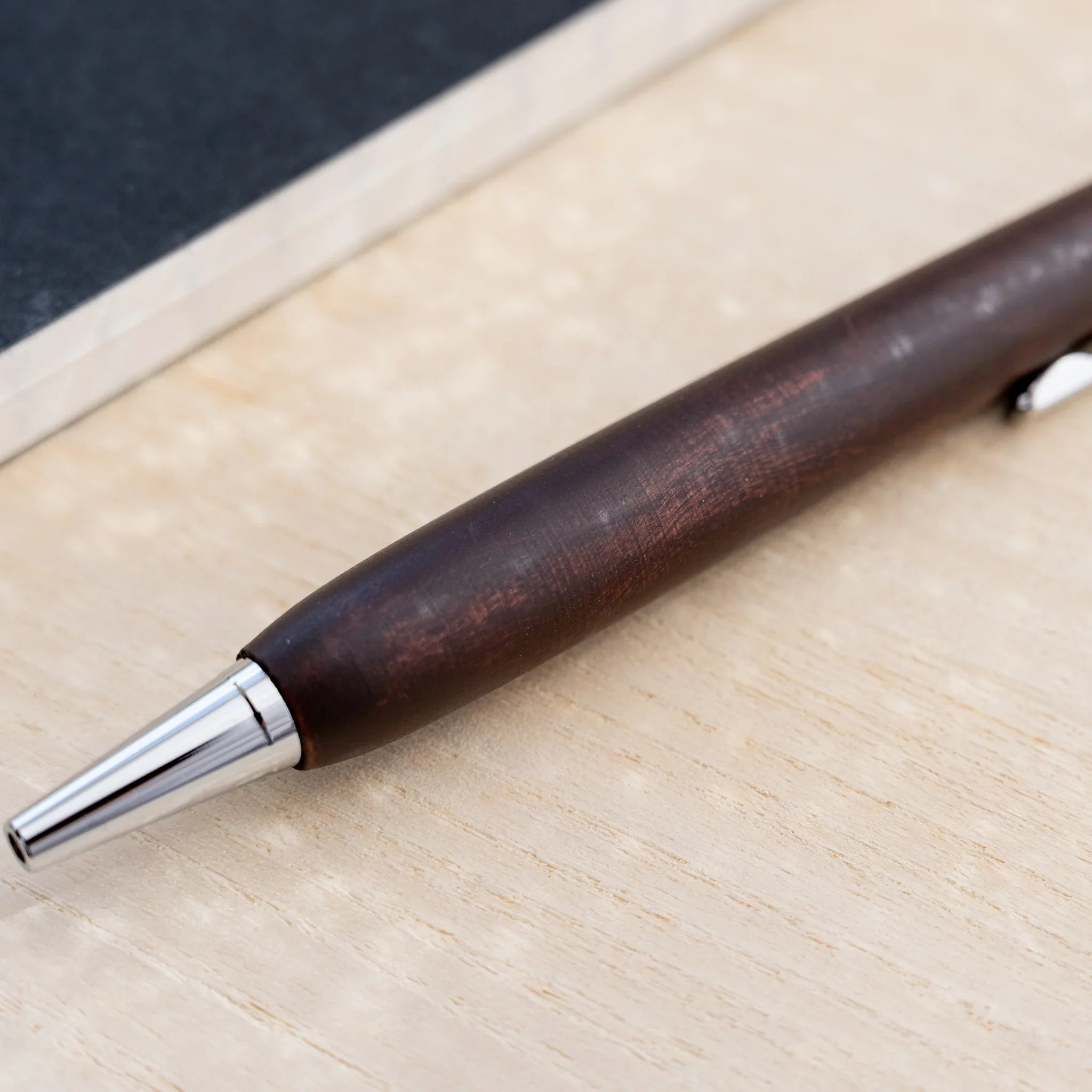 Chocolate brown horse chestnut wood urushi ballpoint pen, close-up of barrel and silver cone tip, Japanese wood