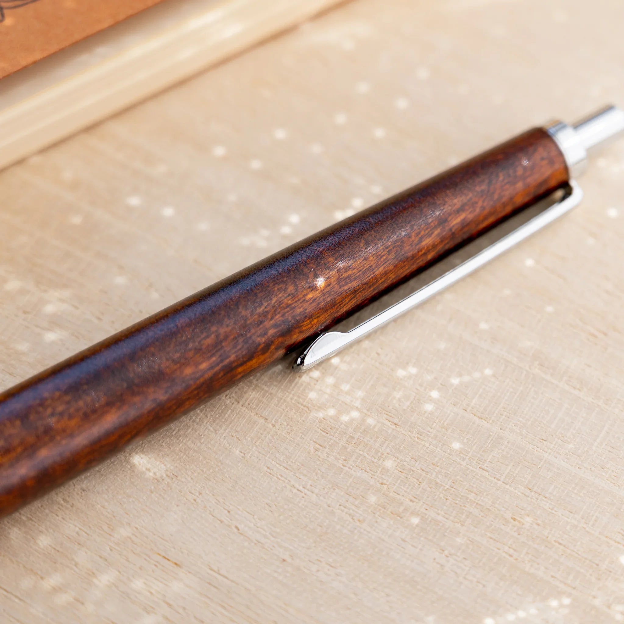 Amber-brown horse chestnut wood urushi ballpoint pen, close-up of barrel and silver knock end, Japanese wood