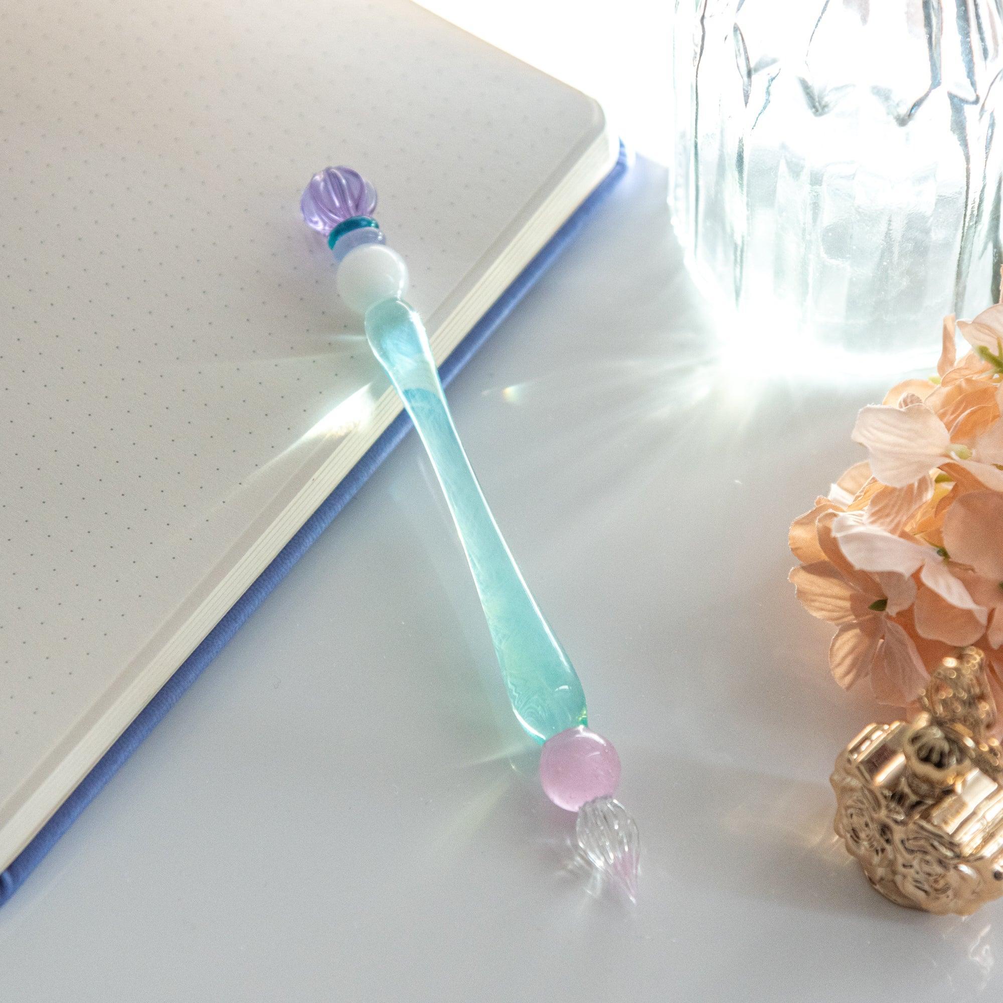 King's Scepter Candy glass dip pen diagonal displayed on white notebook with peach flowers visible below