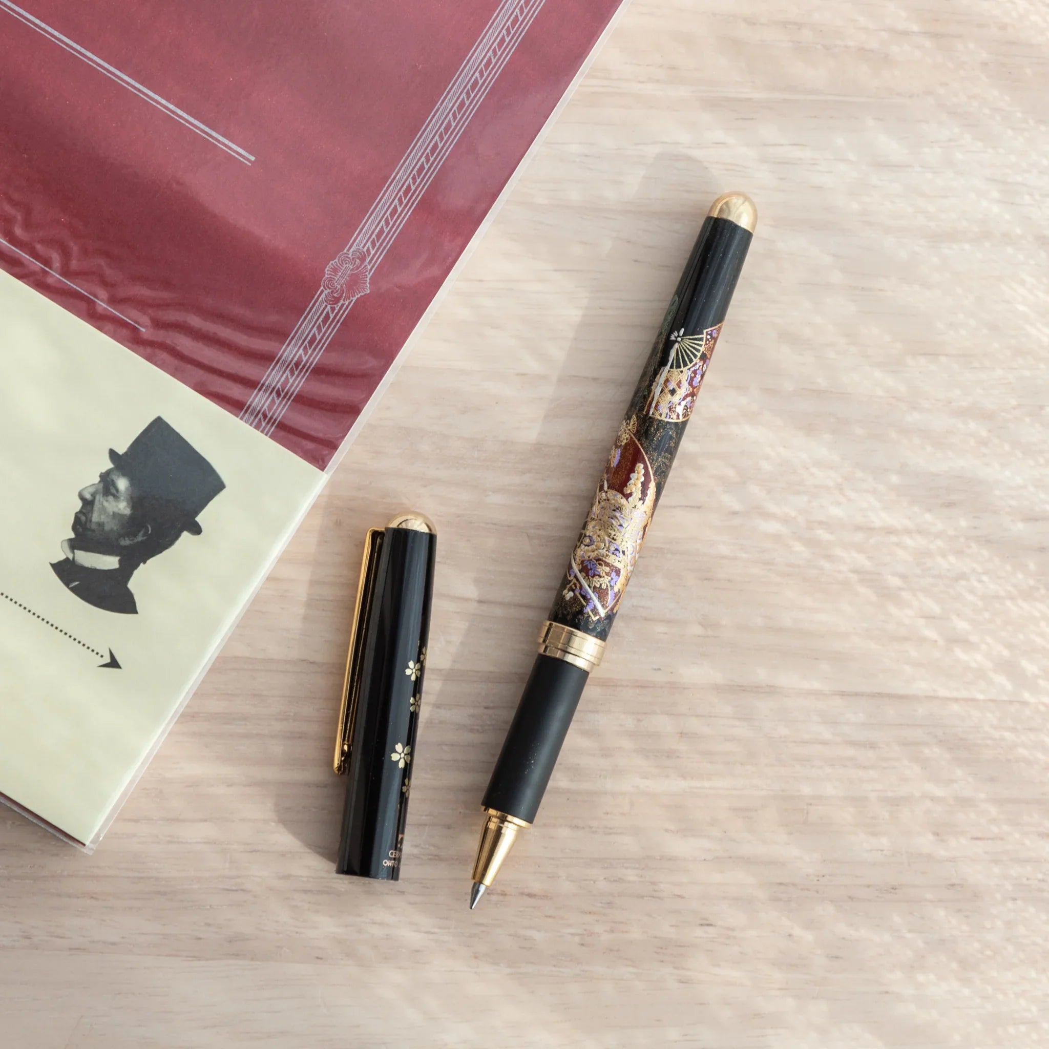 Yamanaka Japanese ballpoint pen uncapped, cap with sakura and gold clip placed separately, body showing maki-e Kyoto motifs