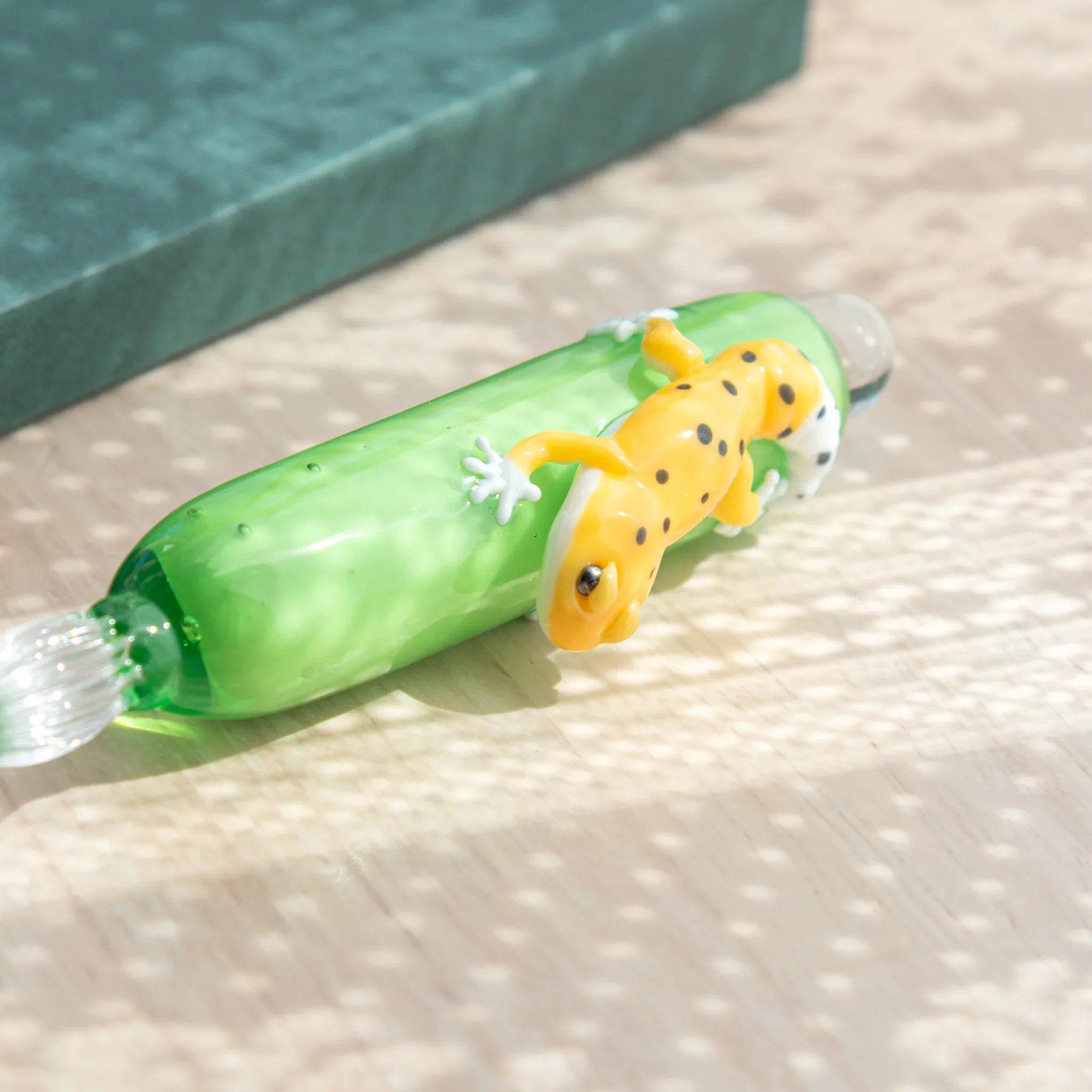 Close-up of yellow spotted leopard gecko figure on green glass dip pen barrel showing white feet and black spot markings
