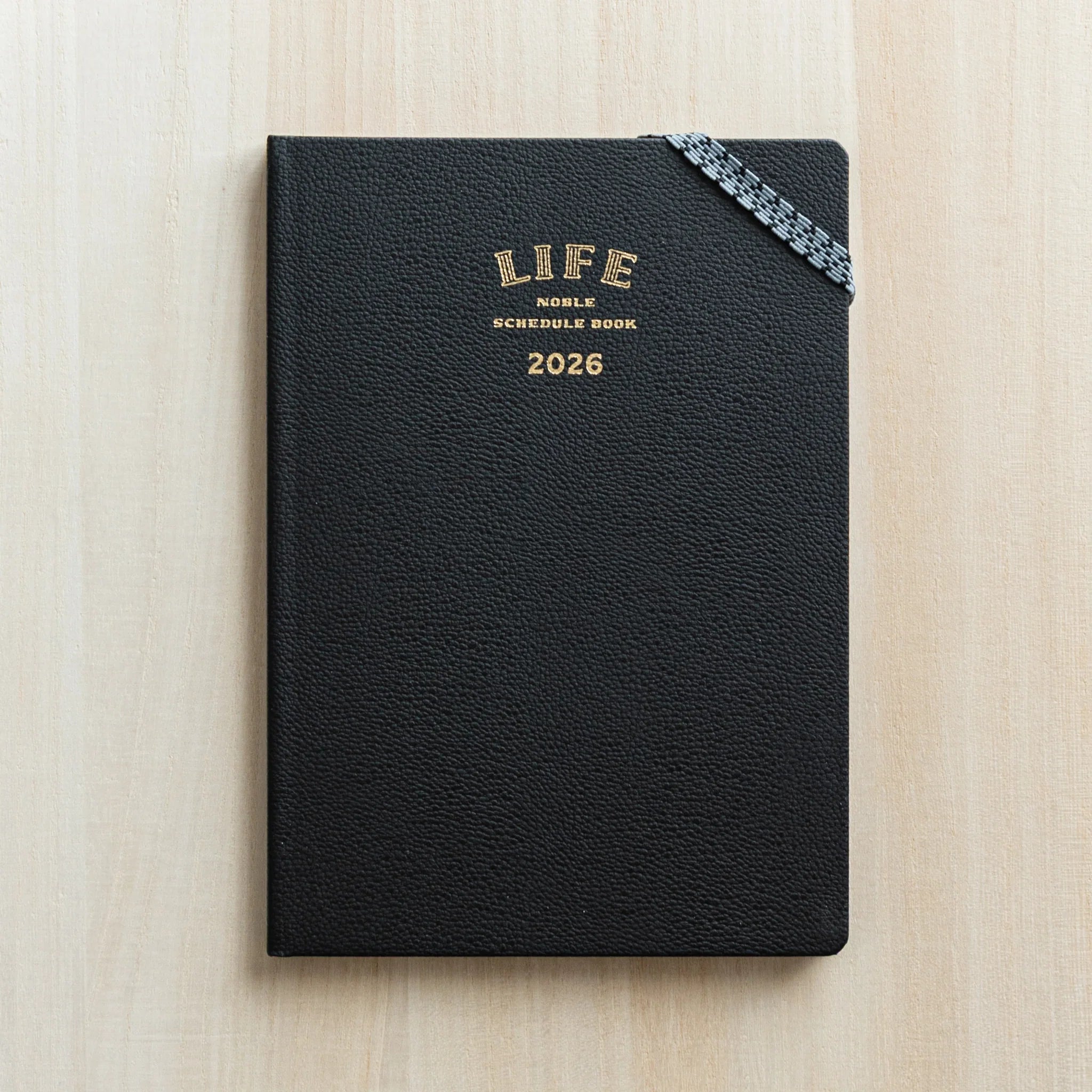 Life Noble 2026 hardcover planner, navy leather cover, open showing pages highlighting gold lettering         