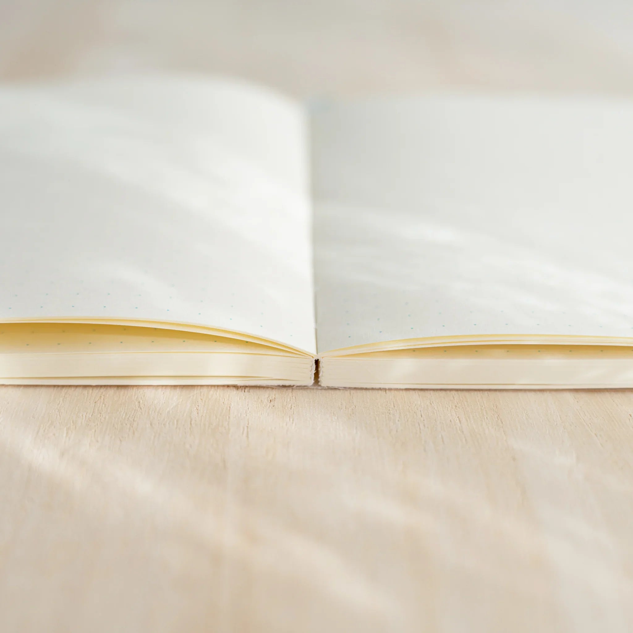 Midori MD Notebook A6 open from side angle showing thread-stitched spine, blank ivory pages lying flat on wooden surface