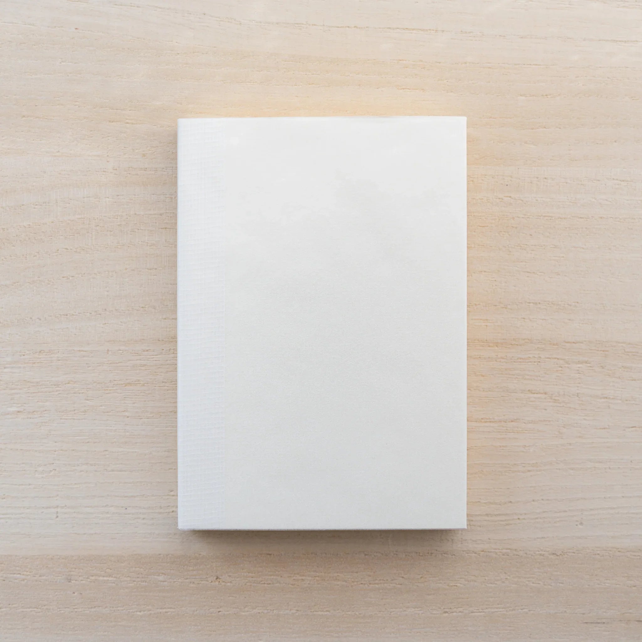 Cream MD Notebook A7, closed blank front cover on a wood surface
