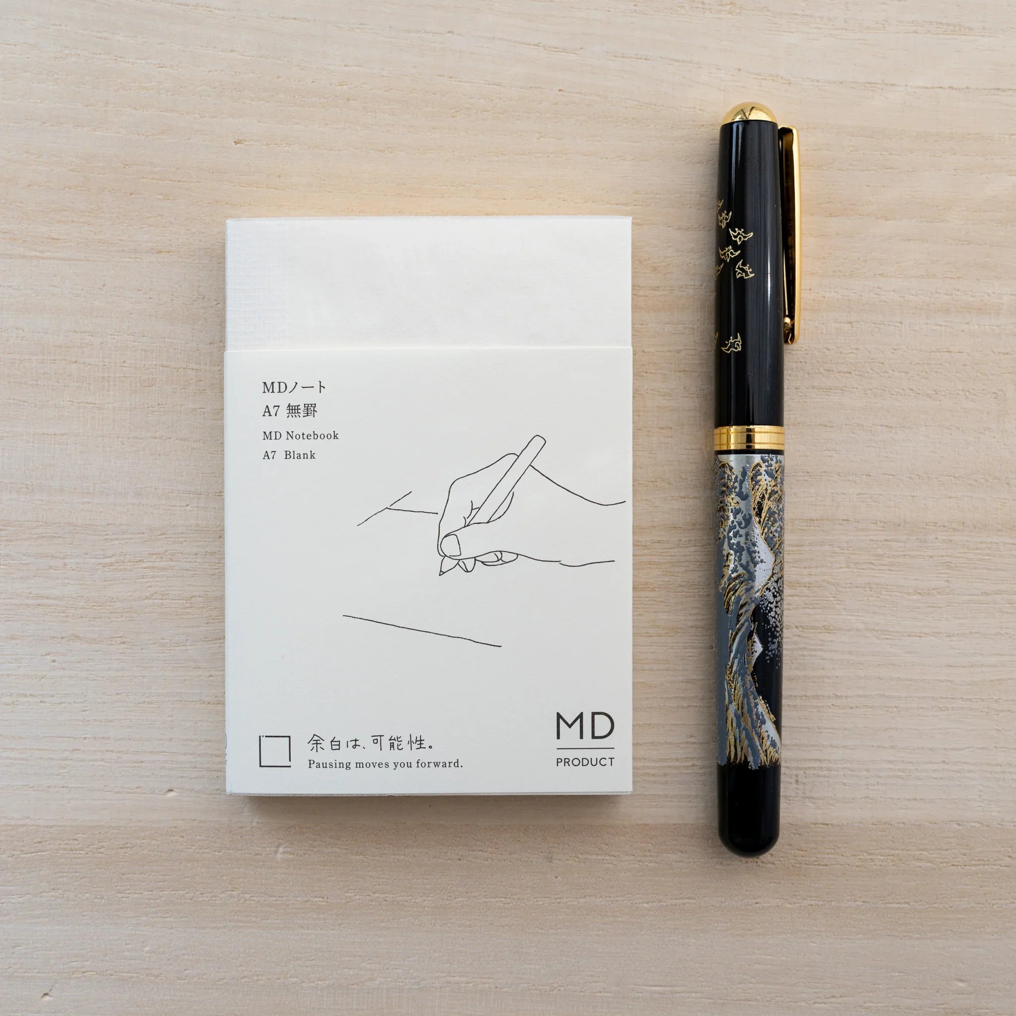 MD Notebook A7 in cream cover with belly band beside a marbled fountain pen on a wood surface