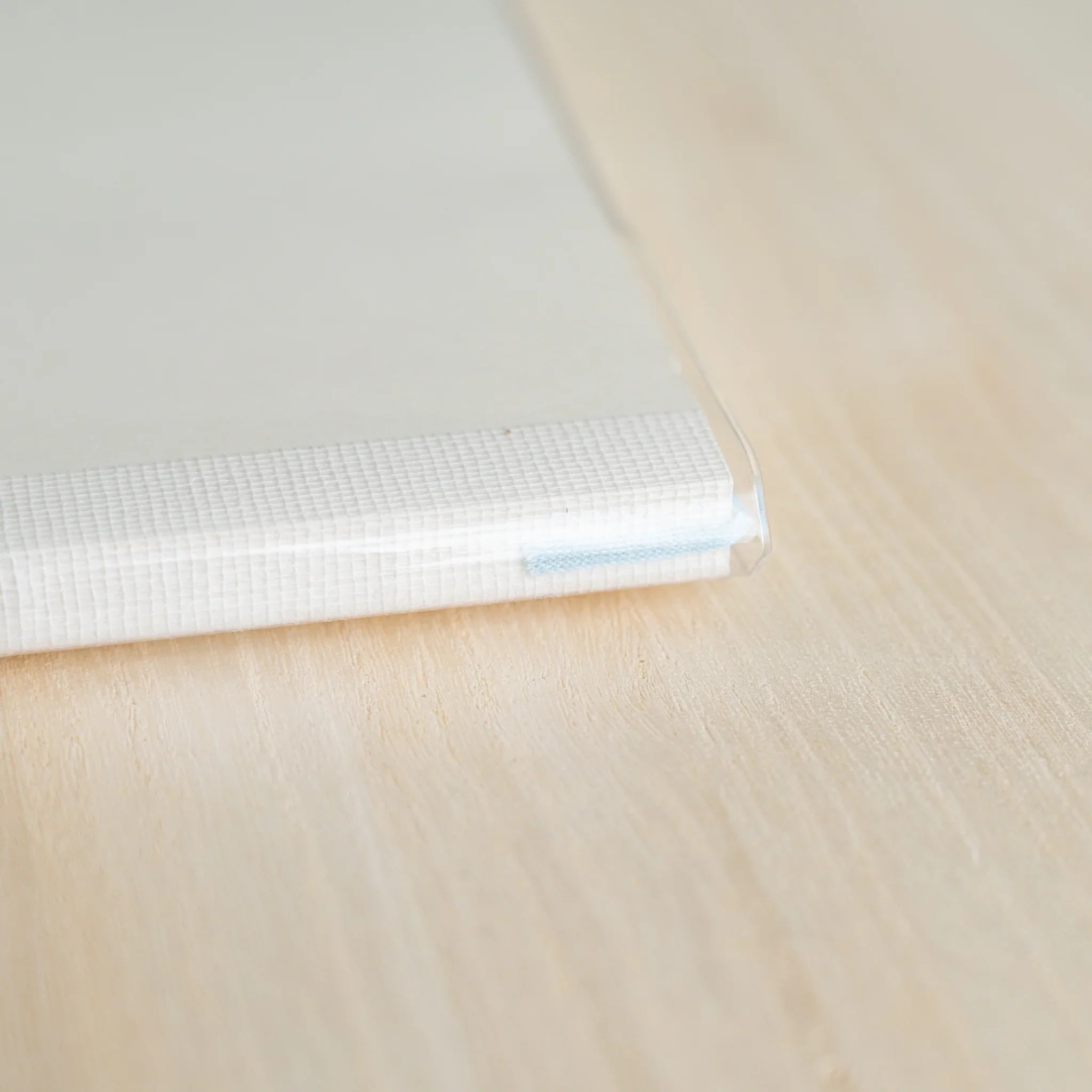 Close-up of the bottom edge of a white MD notebook in clear PVC cover showing textured binding