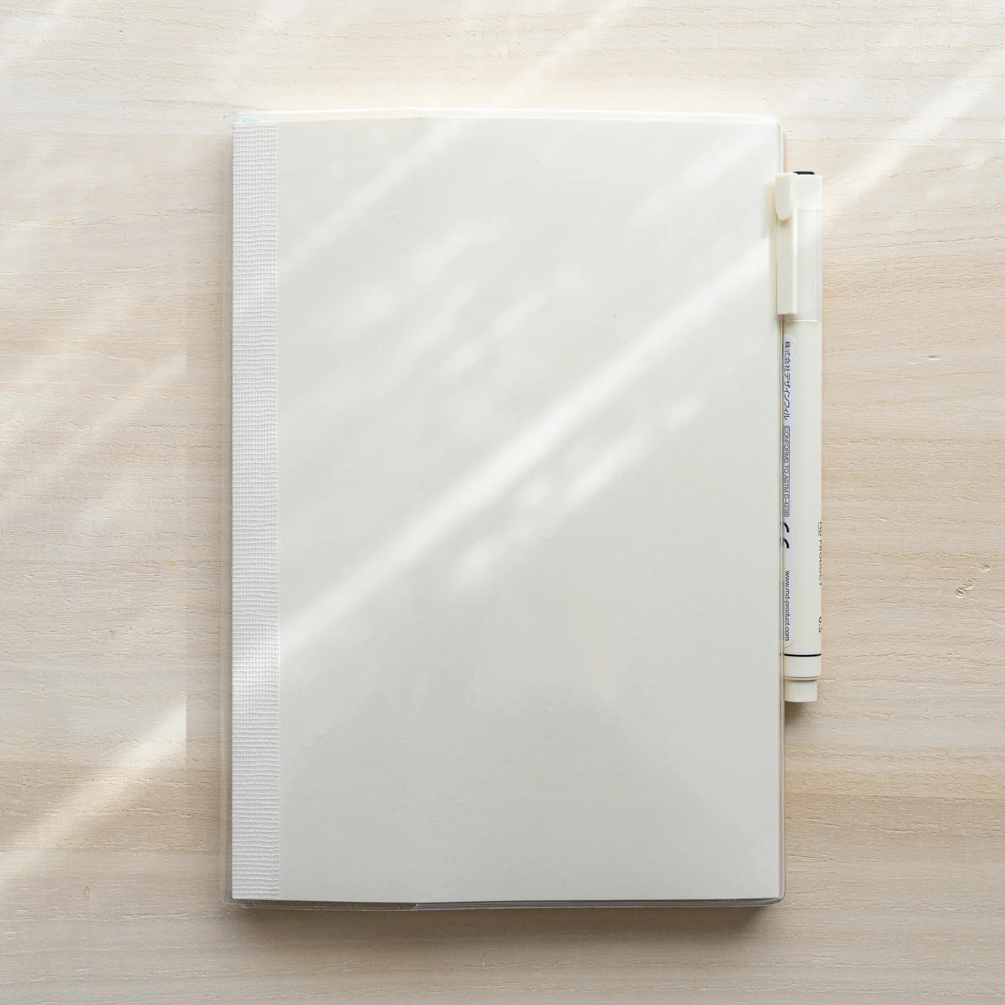 White MD notebook in clear PVC cover with a white MD PRODUCT pen held in the right-side pen holder