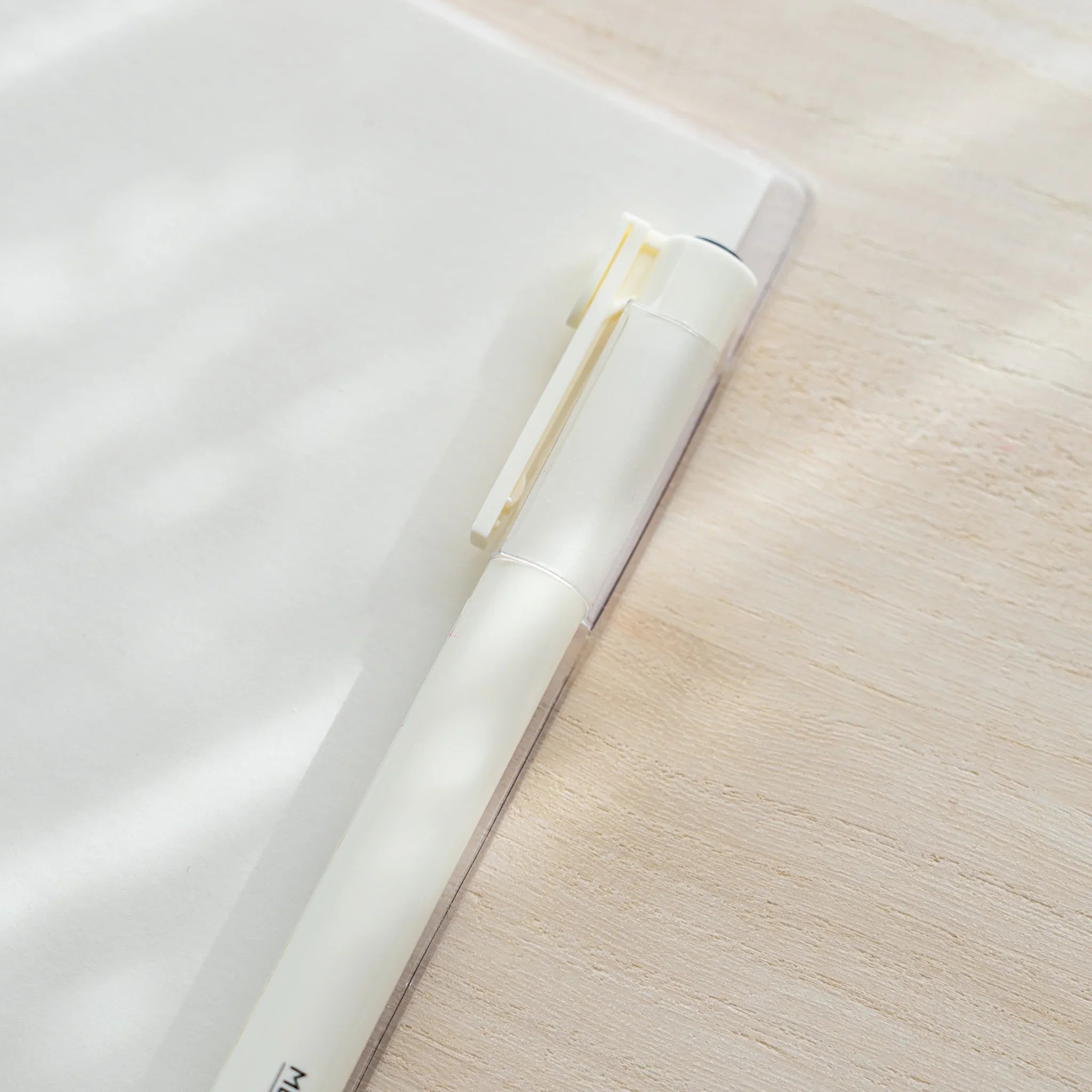 Close-up of a white MD PRODUCT pen in the pen holder slot of a clear PVC Midori MD Notebook Cover