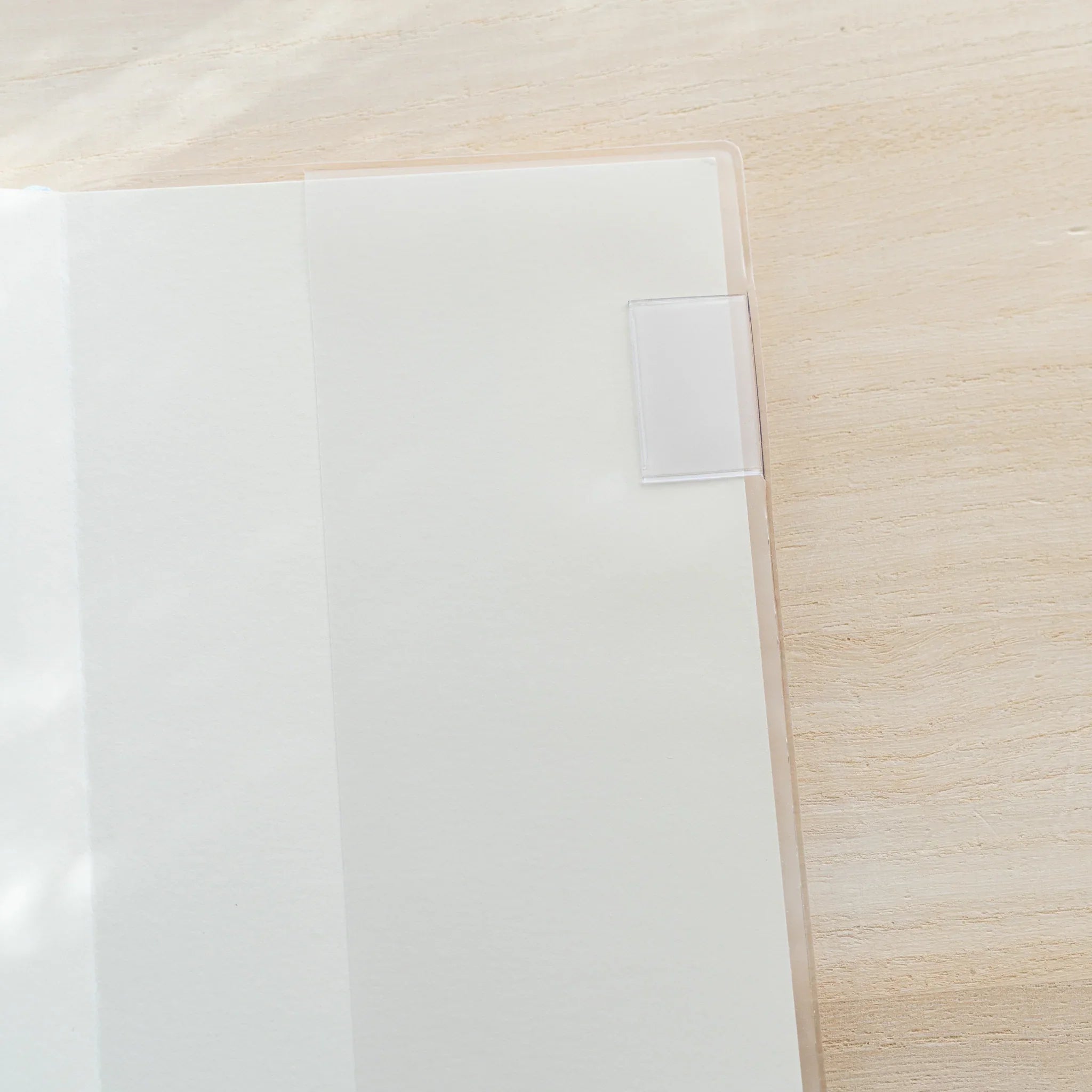 Clear PVC Midori MD Notebook Cover opened flat showing two transparent panels on a wood surface