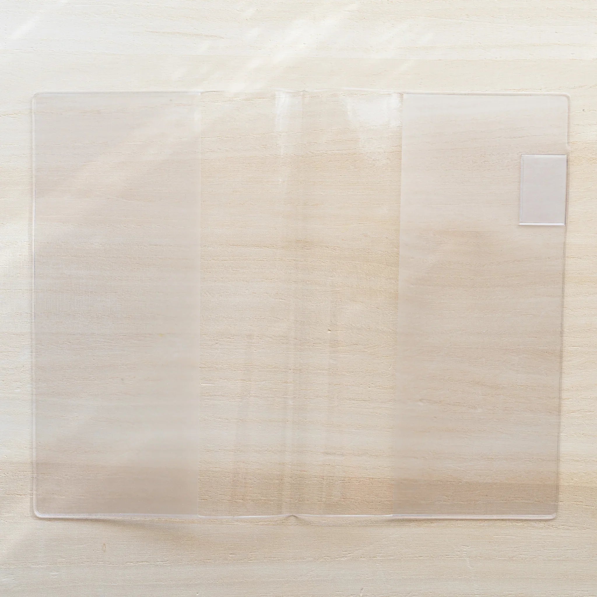 Clear PVC Midori MD Notebook Cover laid flat, transparent with a small white bookmark tab