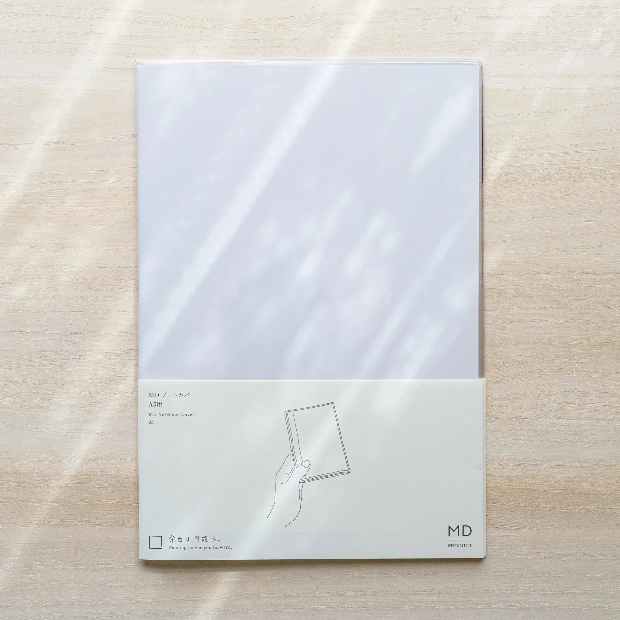 Midori MD Notebook Cover A5 in packaging, clear PVC cover with paper band and size label on wood