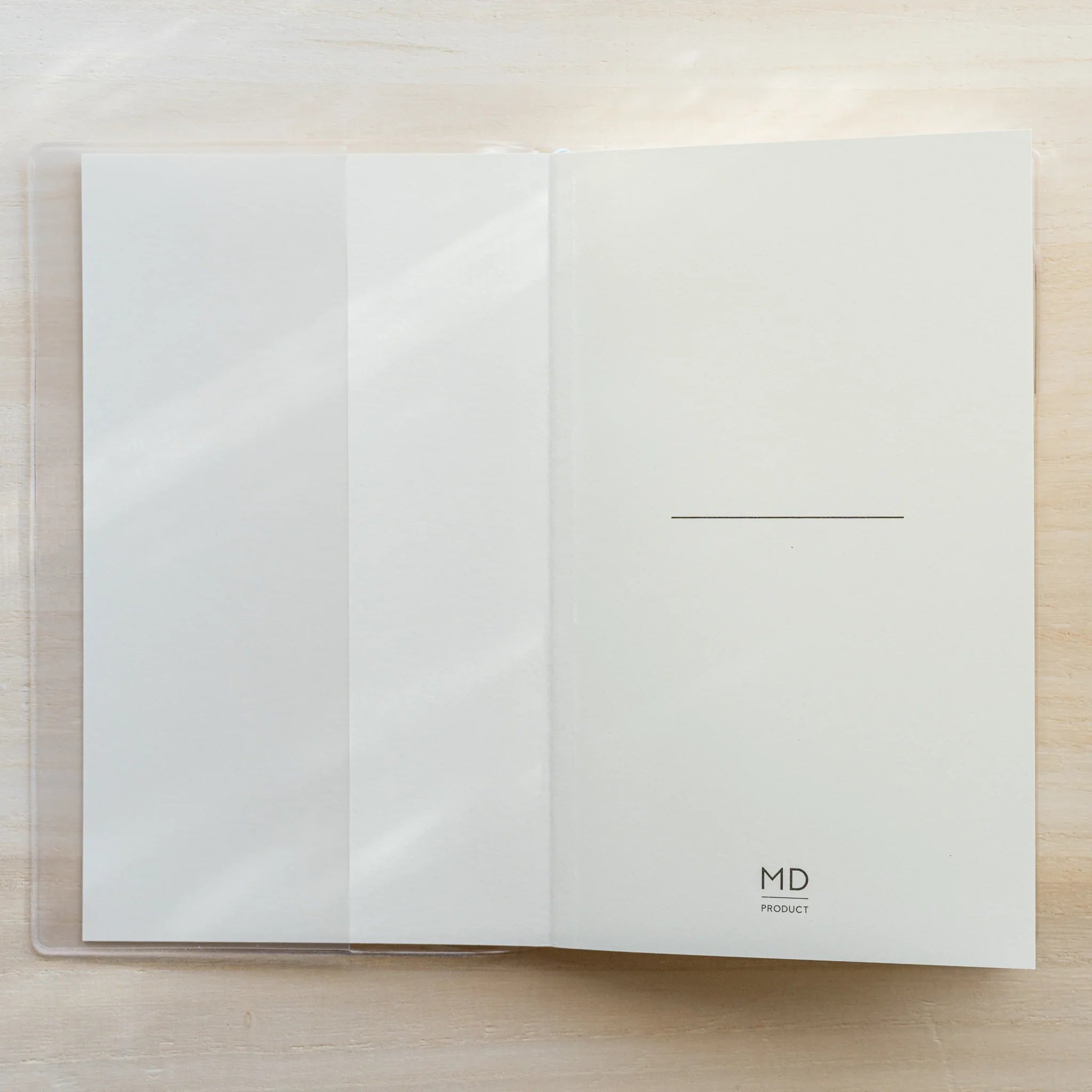 Clear PVC Midori MD Notebook Cover laid flat on a wood surface with a center fold line