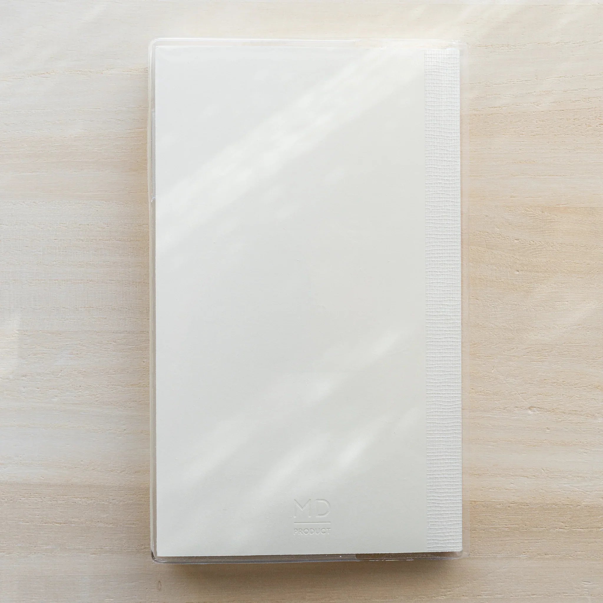 Slim white MD notebook inside a clear PVC Midori MD Notebook Cover, closed front view
