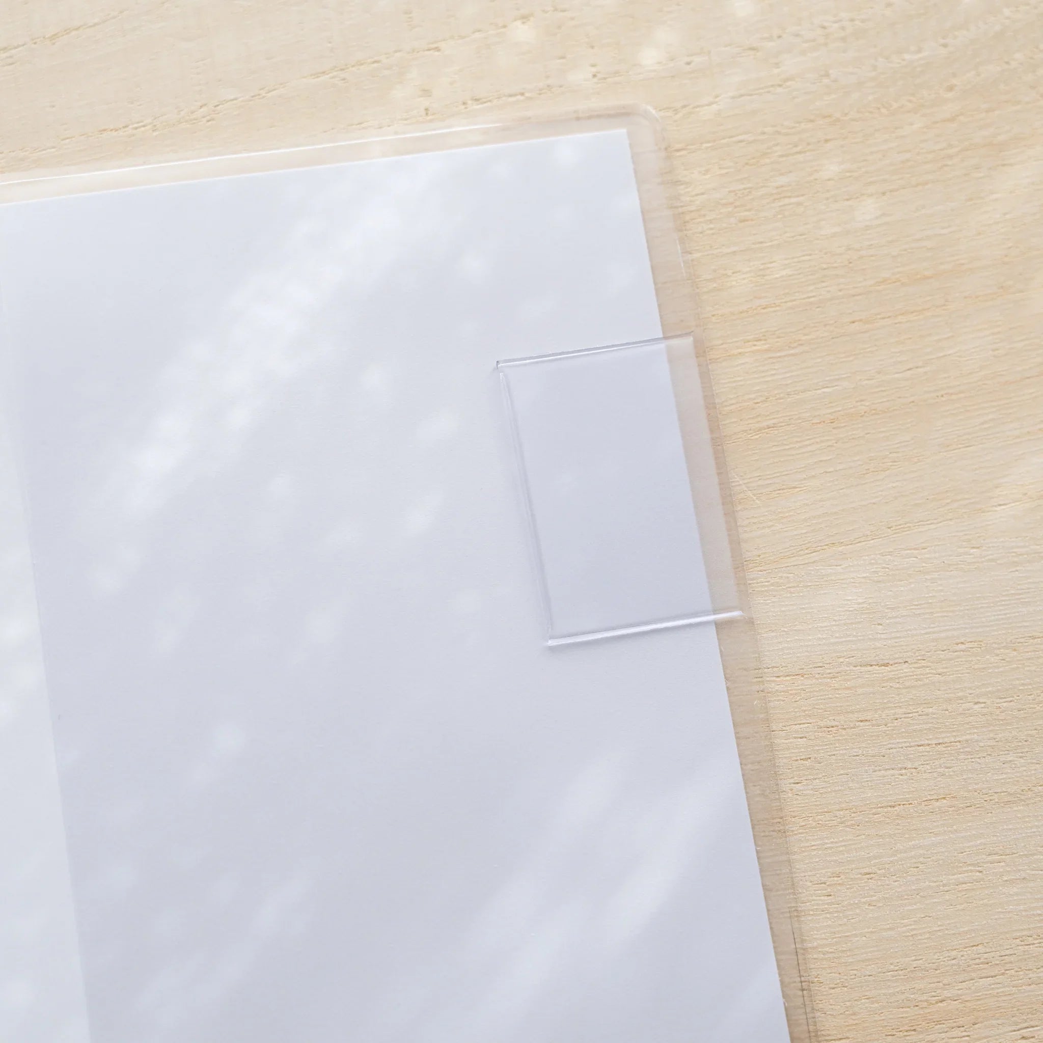 MD Notebook Cover opened flat in clear PVC, blank white two-page spread on a wood surface