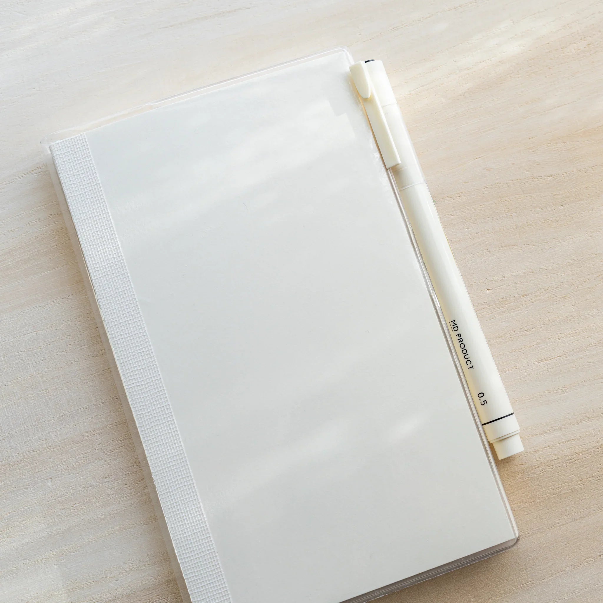 White MD PRODUCT pen resting diagonally across a clear PVC Midori MD Notebook Cover