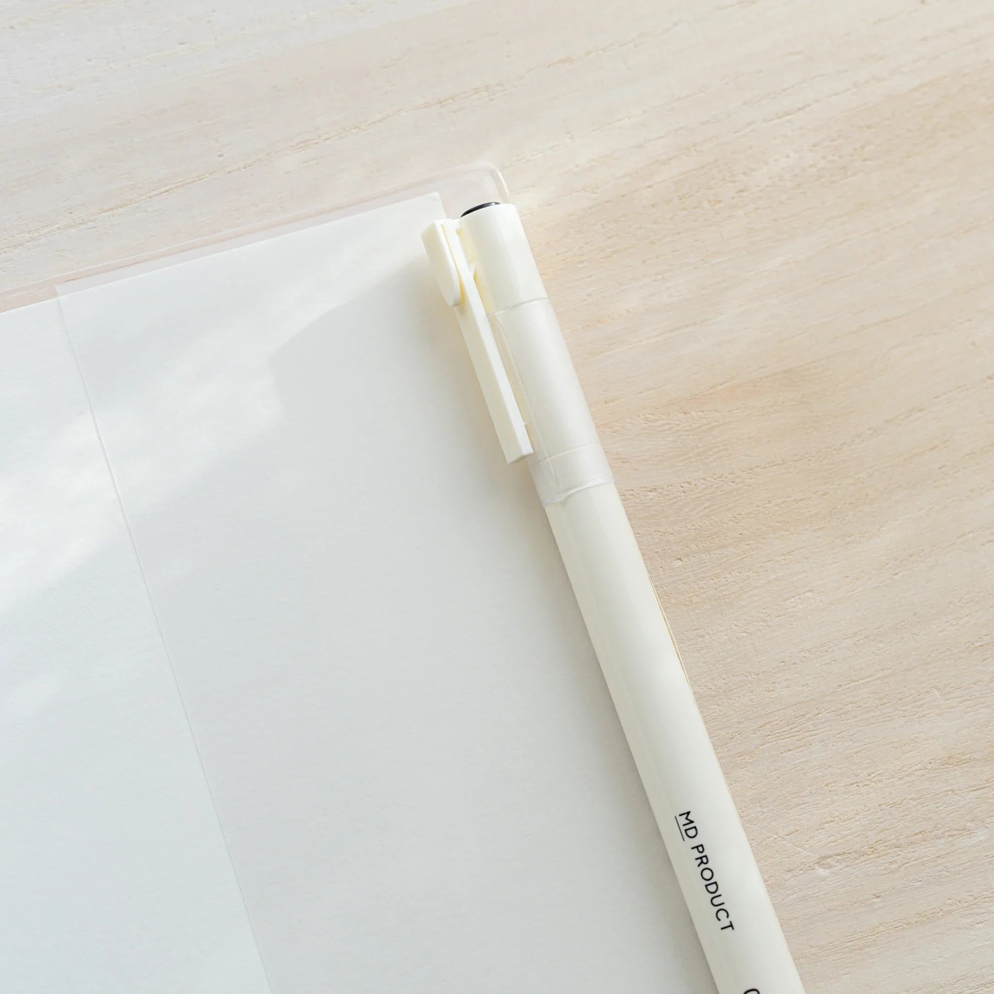Close-up of a white MD PRODUCT pen resting across the corner of a clear PVC cover