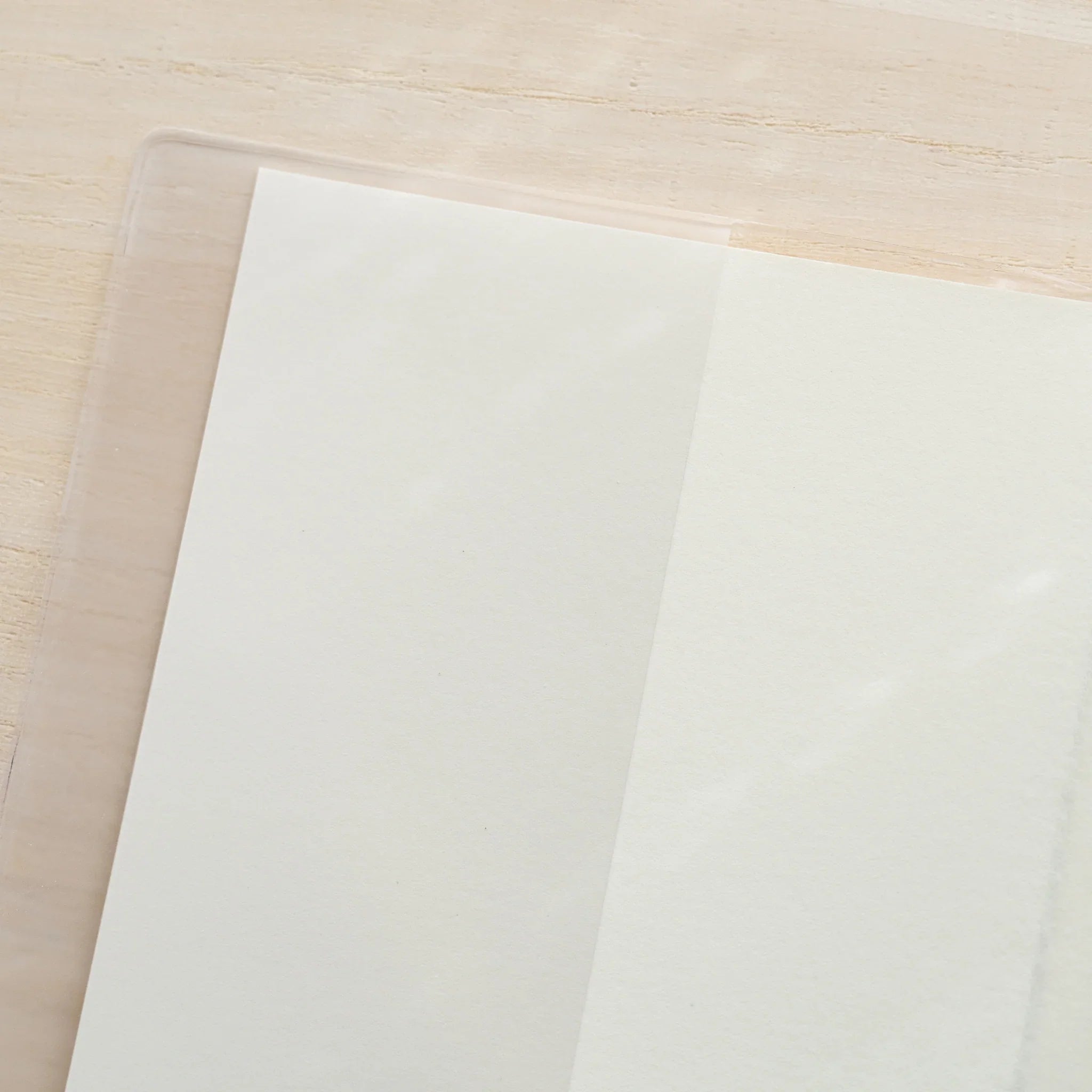 Close-up of a clear PVC Midori MD Notebook Cover corner overlapping a white notebook page