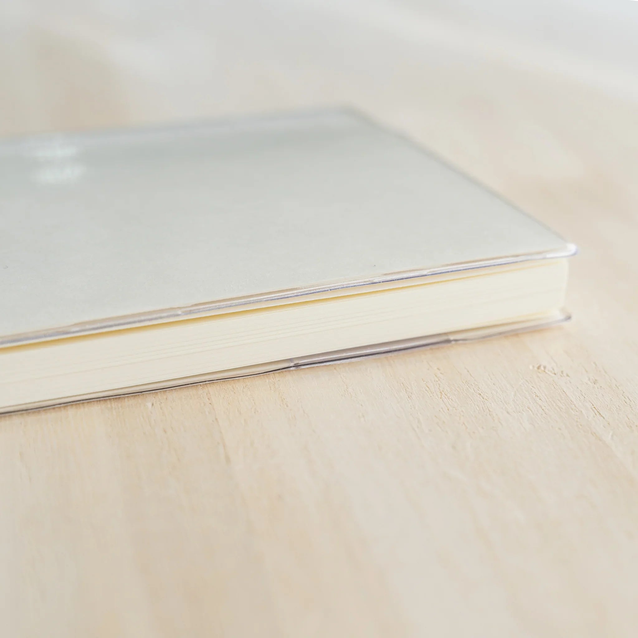 White MD notebook inside a clear PVC Midori MD Notebook Cover, closed three-quarter view