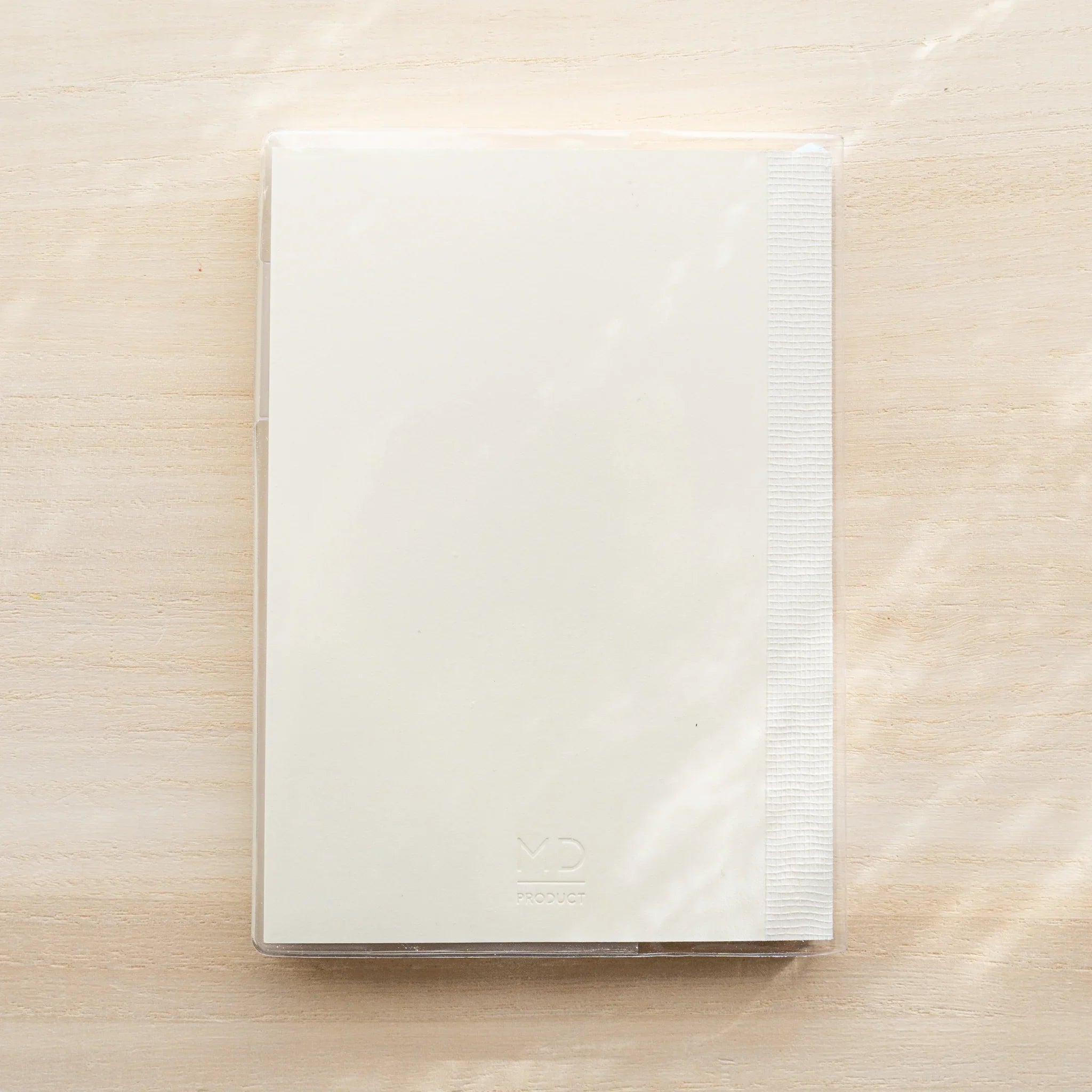 White MD notebook inside clear PVC Midori MD Notebook Cover, closed front view on wood