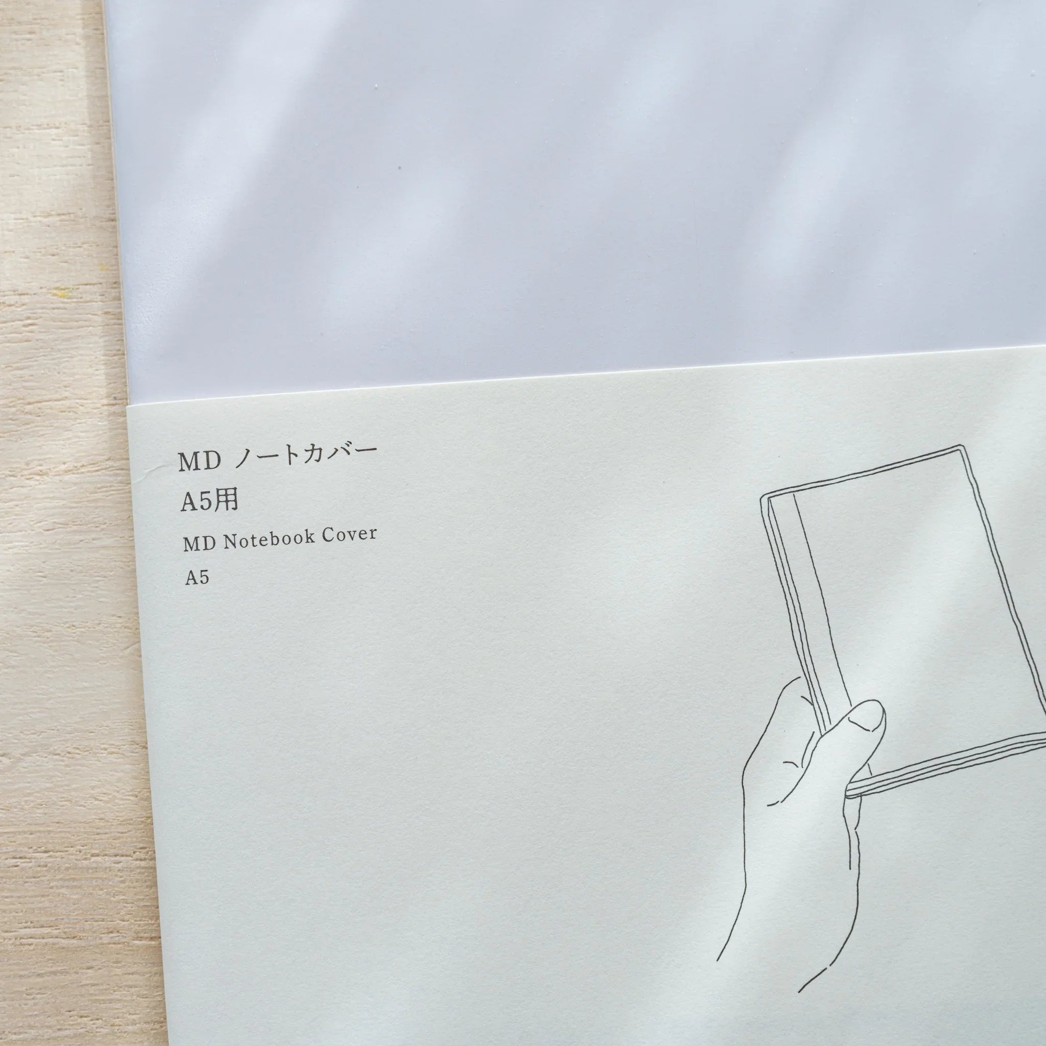 Insert card for Midori MD Notebook Cover A5 with line drawing of a hand holding a covered notebook