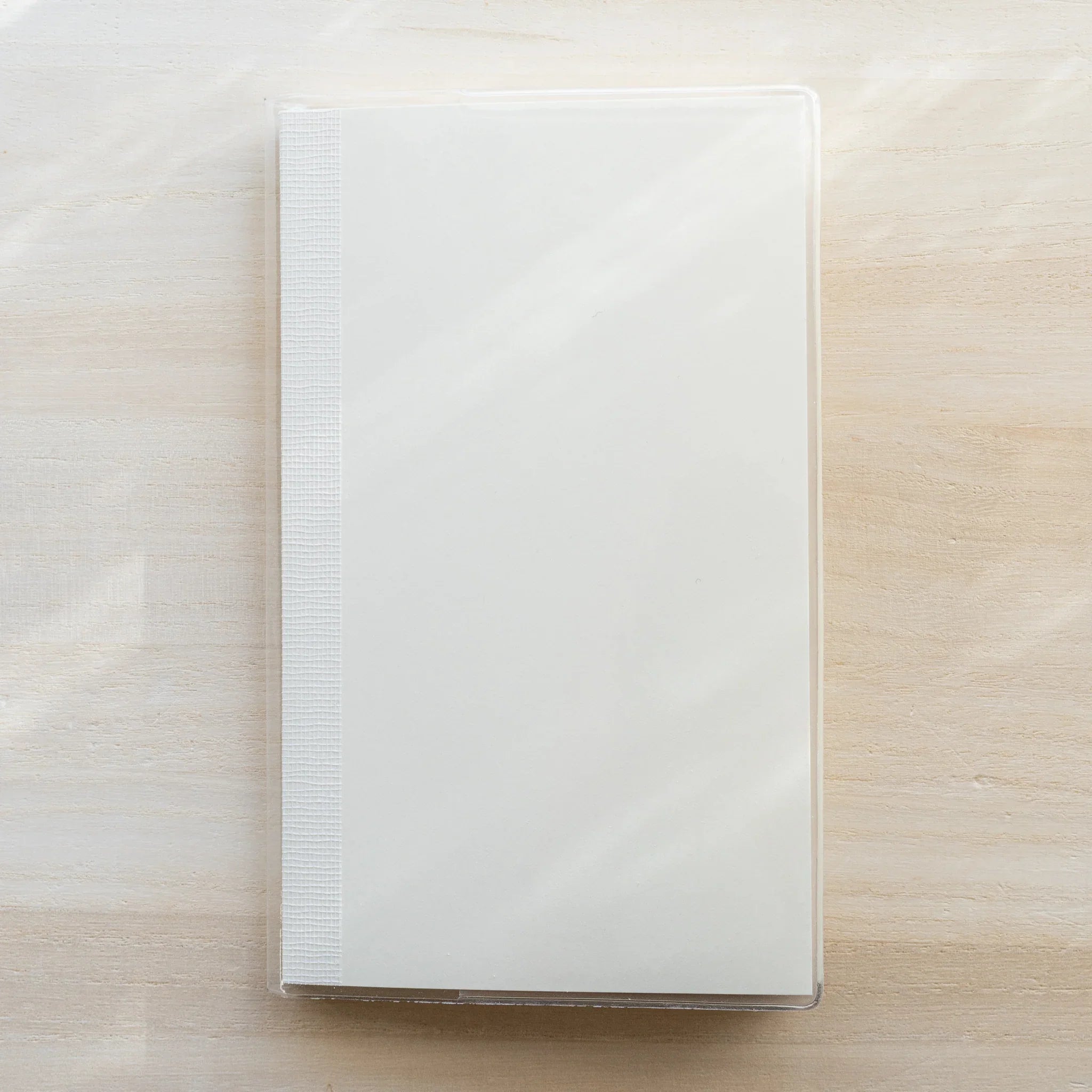 Clear PVC Midori MD Notebook Cover on a white notebook laid flat with a center fold line