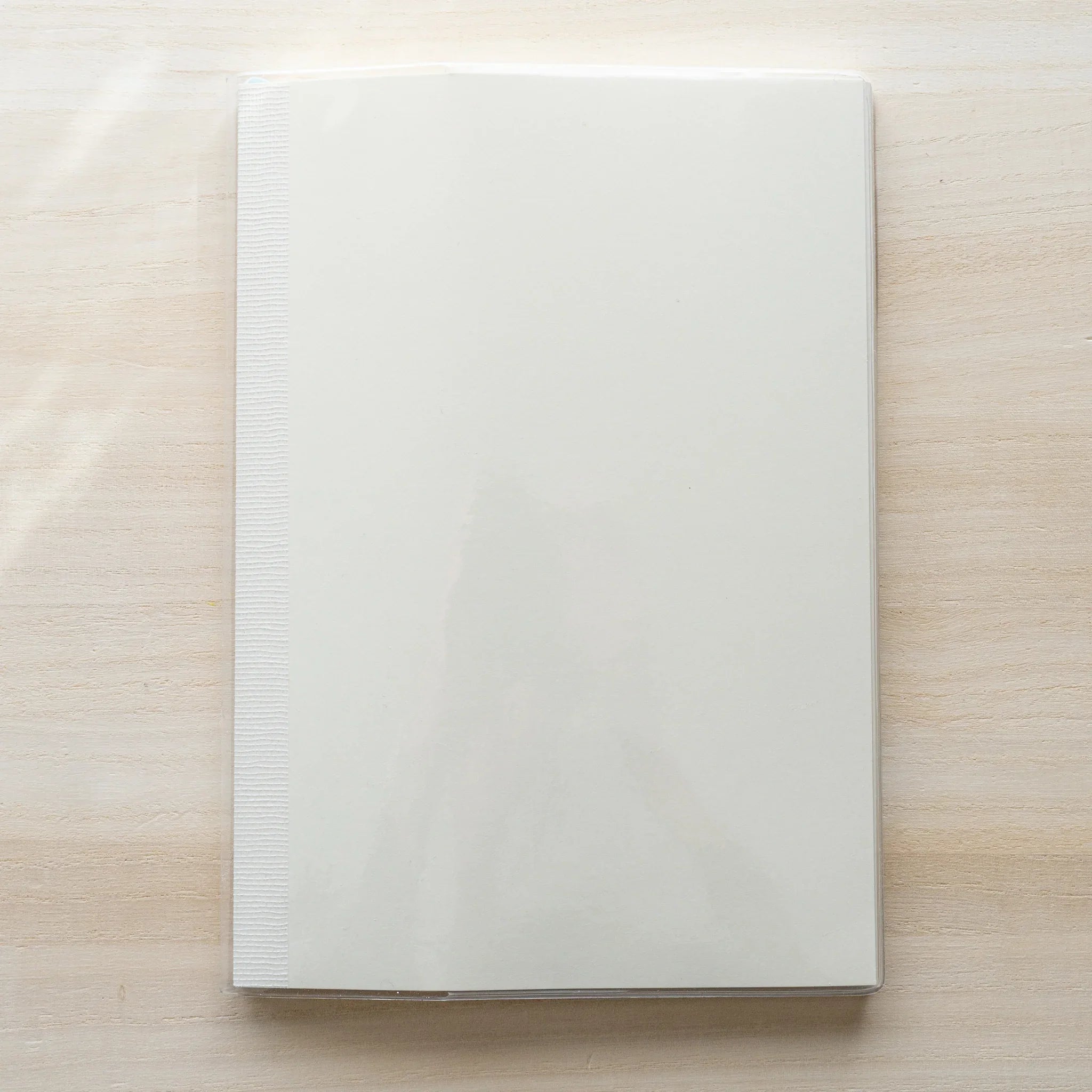 White MD notebook inside a clear PVC Midori cover, closed front view on a wood surface