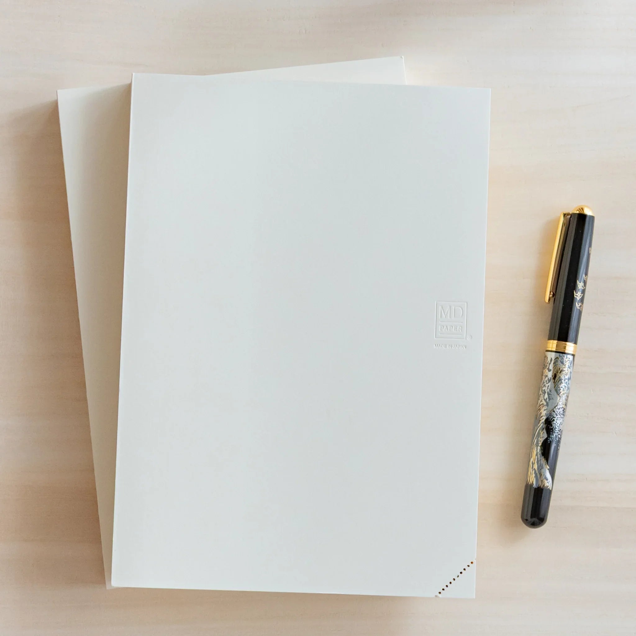 Midori MD Notebook, white front cover with embossed MD Paper Made in Japan logo, black fountain pen on light wood